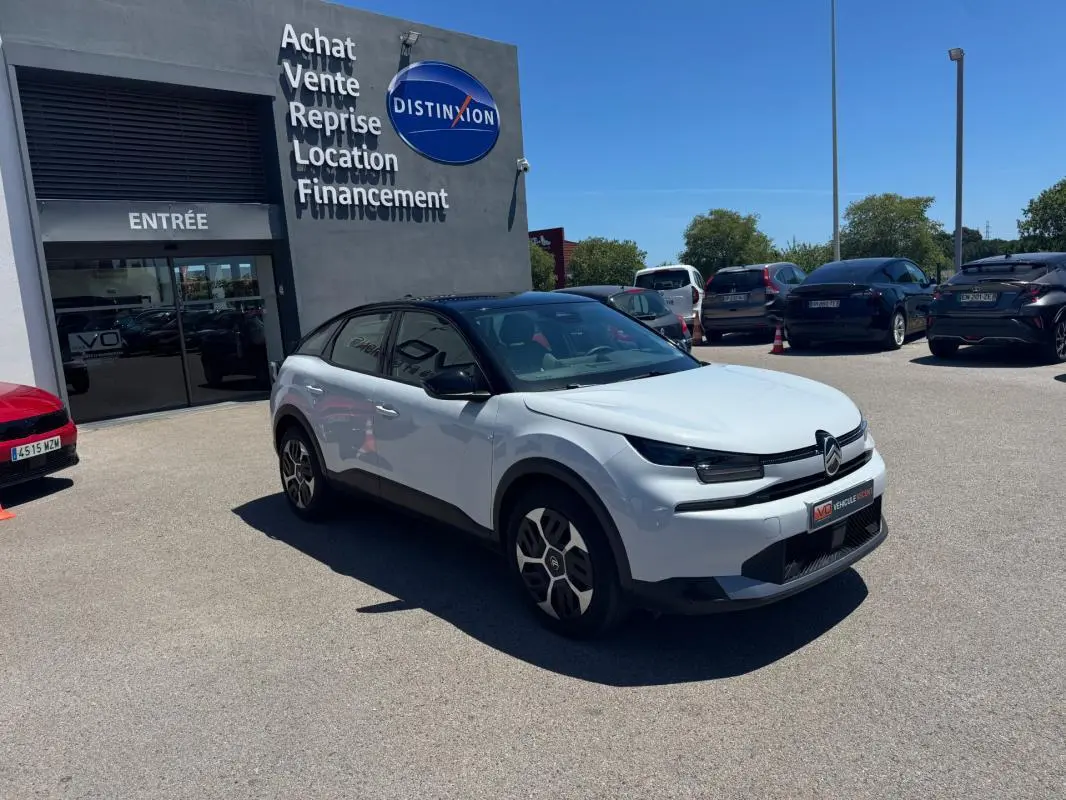Citroën C4 hybride blanc vue 3/4 avant droit, avec toit noir et jantes alliage 18 pouces, stationnée devant un showroom.