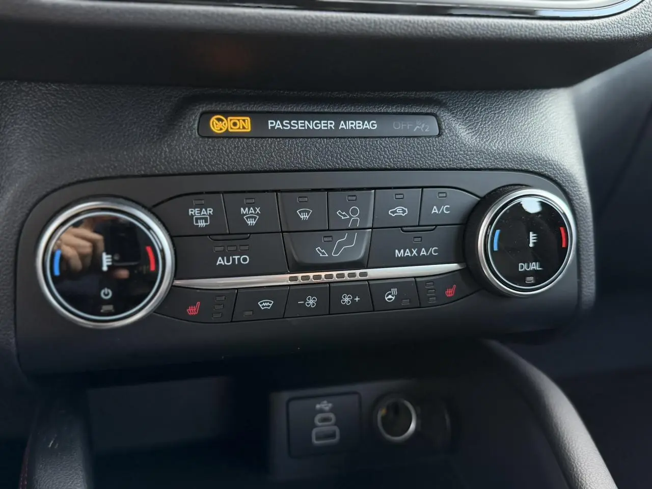 Gros plan sur la console de climatisation du Ford Kuga noir, avec commandes chauffantes et affichage airbag passager.