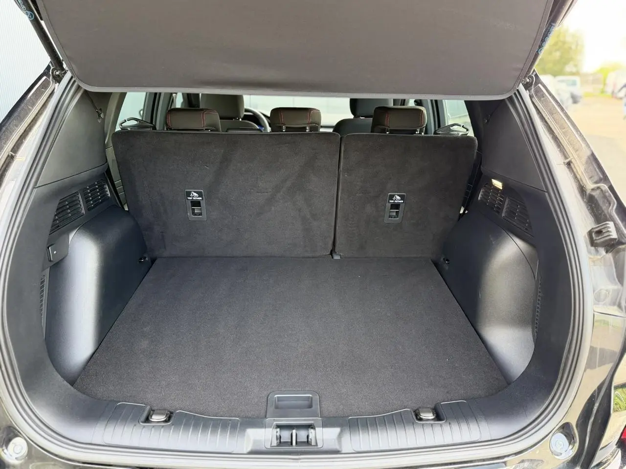 Coffre ouvert d’un Ford Kuga noir Agathe, vue arrière montrant l’espace de chargement et les dossiers de sièges arrière.