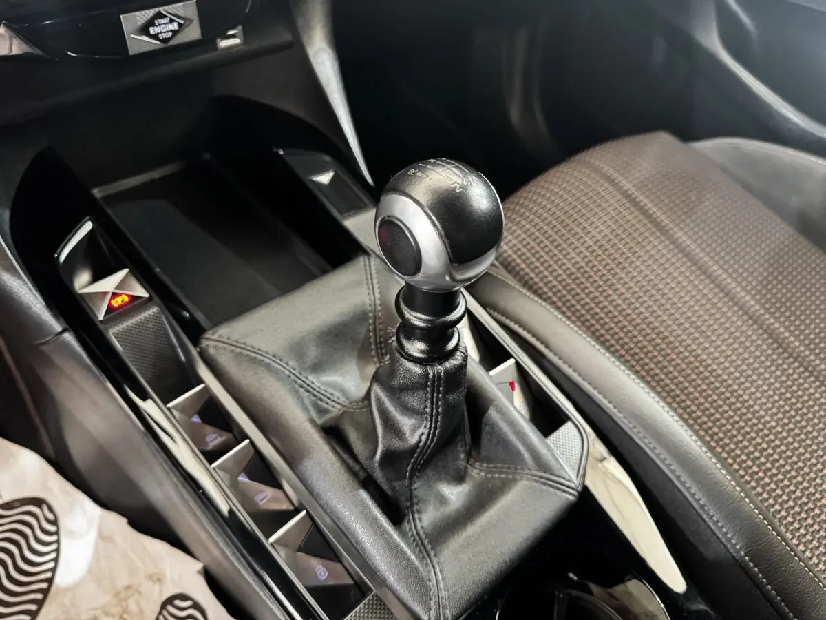 Gros plan sur le levier de vitesse manuel en cuir noir dans l’habitacle du DS3 Crossback gris foncé, siège tissu à motifs visible.
