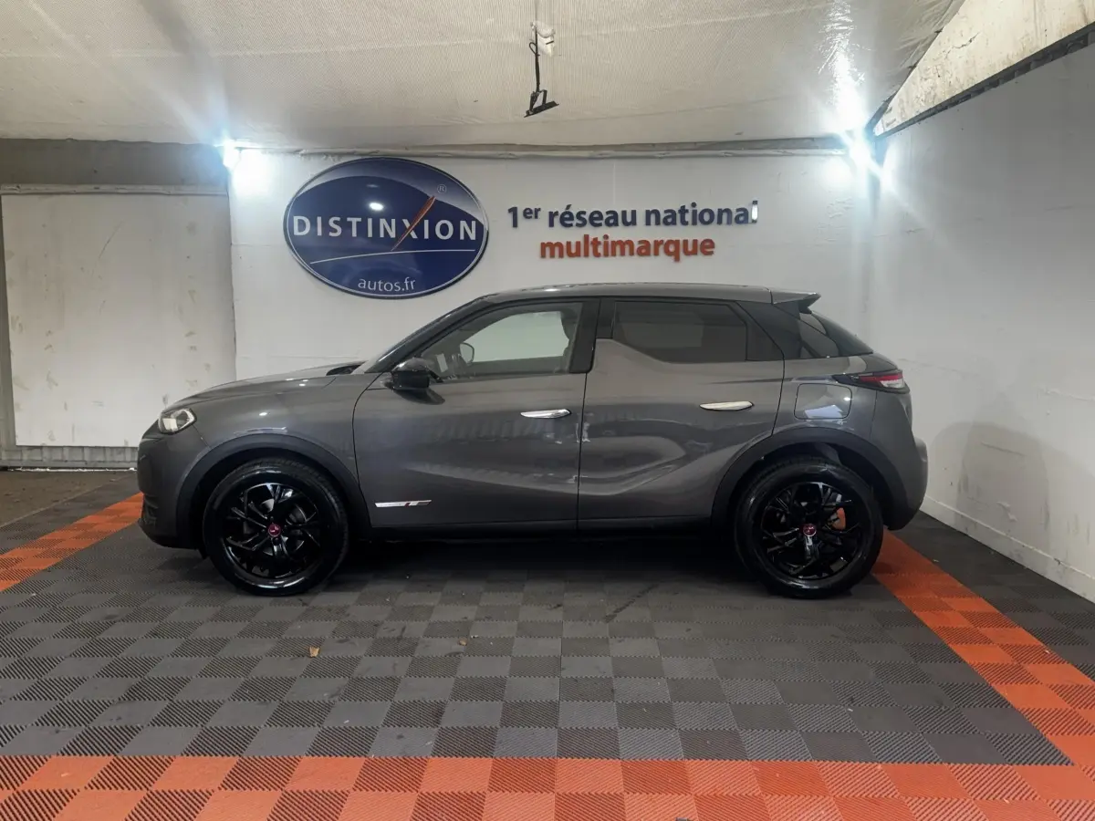 Vue de profil côté gauche d'un DS3 Crossback gris foncé avec jantes noires brillantes dans un showroom.