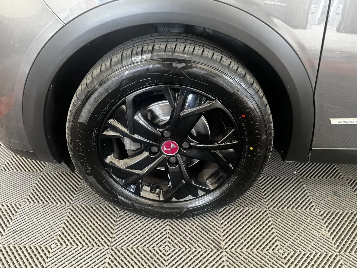 Gros plan sur la roue avant droite noire brillante d’un DS3 Crossback gris foncé avec logo rouge au centre.
