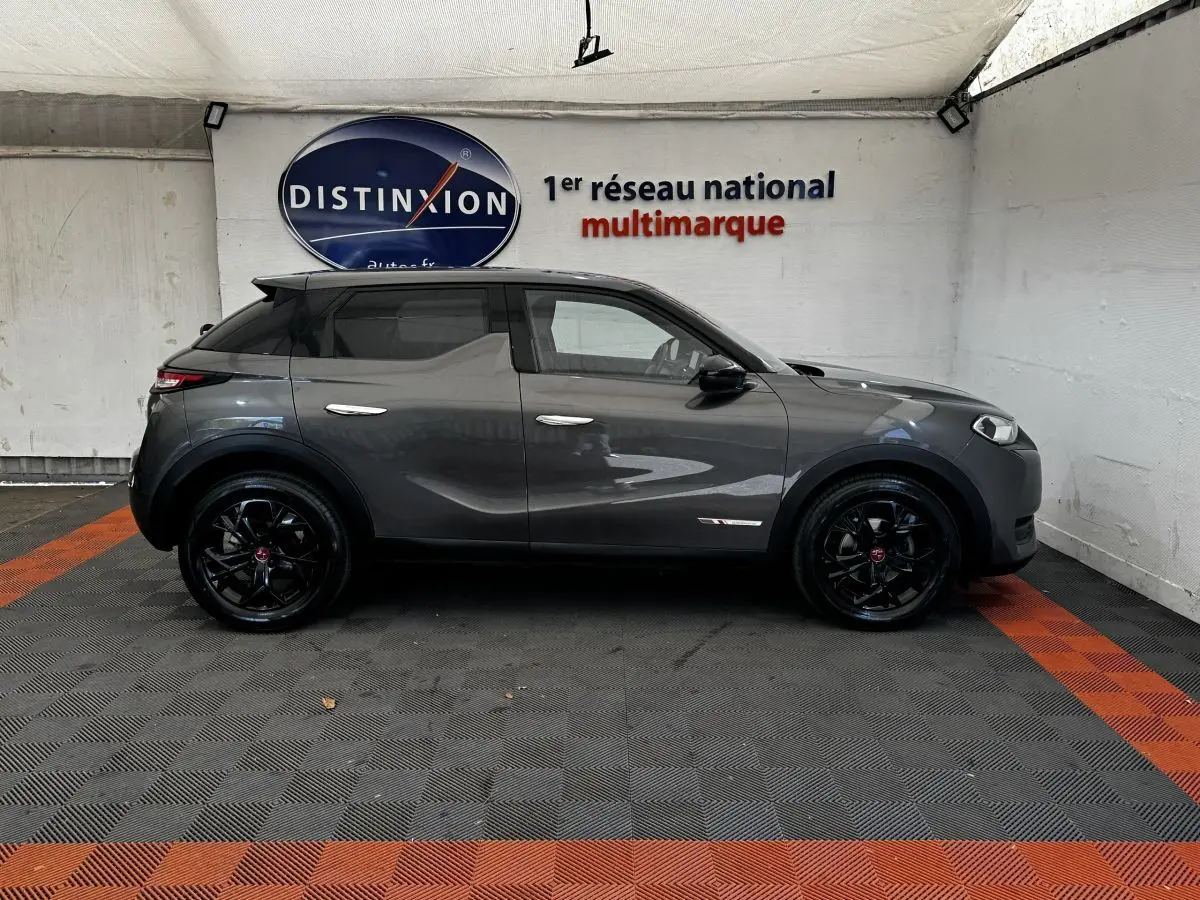 Vue de profil côté gauche d’un DS3 Crossback gris foncé avec jantes noires et toit noir dans un showroom.