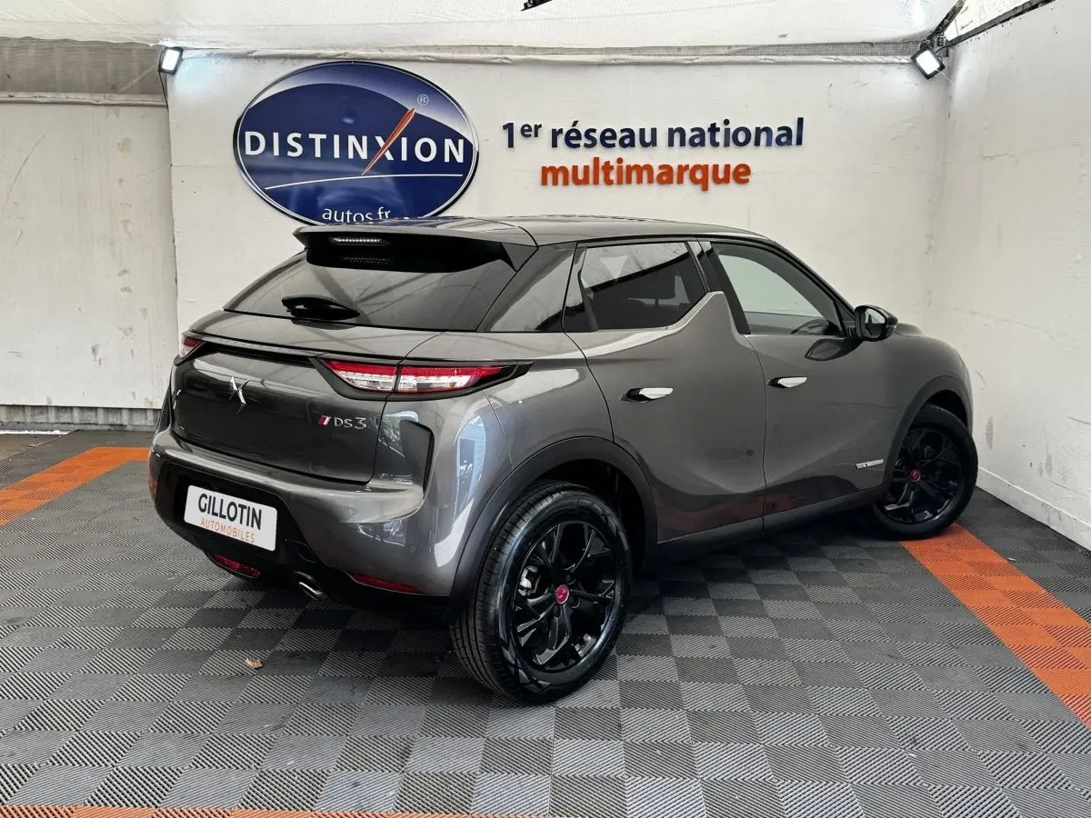 Vue 3/4 arrière droite d'un DS3 Crossback gris foncé avec jantes noires et toit noir dans un showroom.
