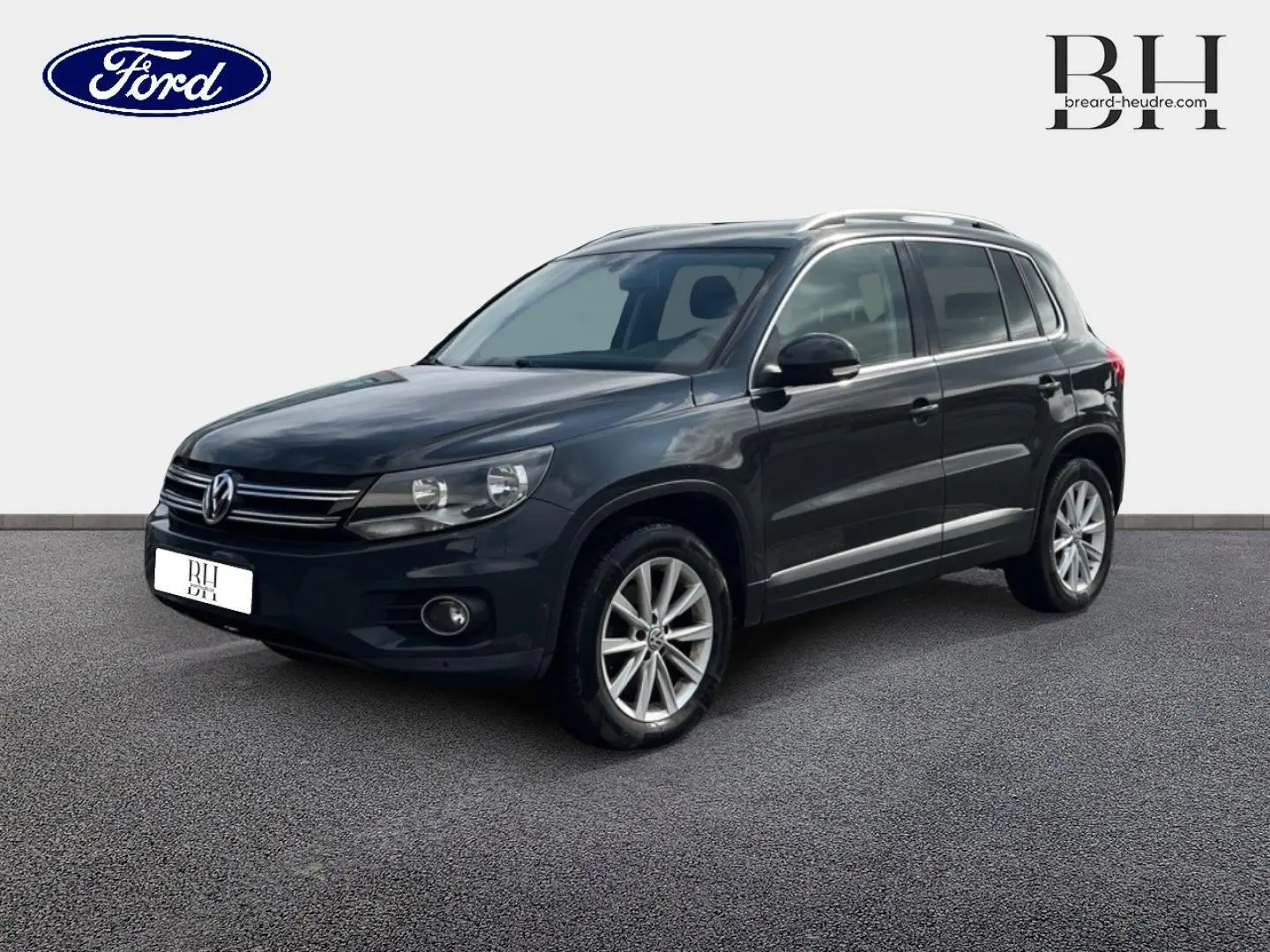 Volkswagen Tiguan gris poivre vu en 3/4 avant droit avec jantes alu et barres de toit visibles.