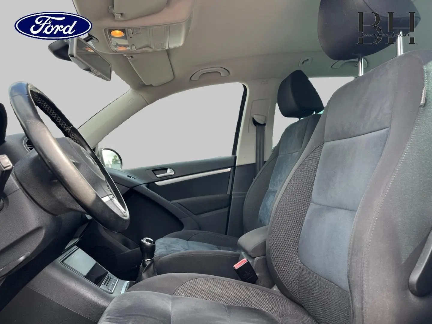Vue intérieure côté conducteur du Volkswagen Tiguan 2014, sièges sport en tissu gris avec volant cuir.