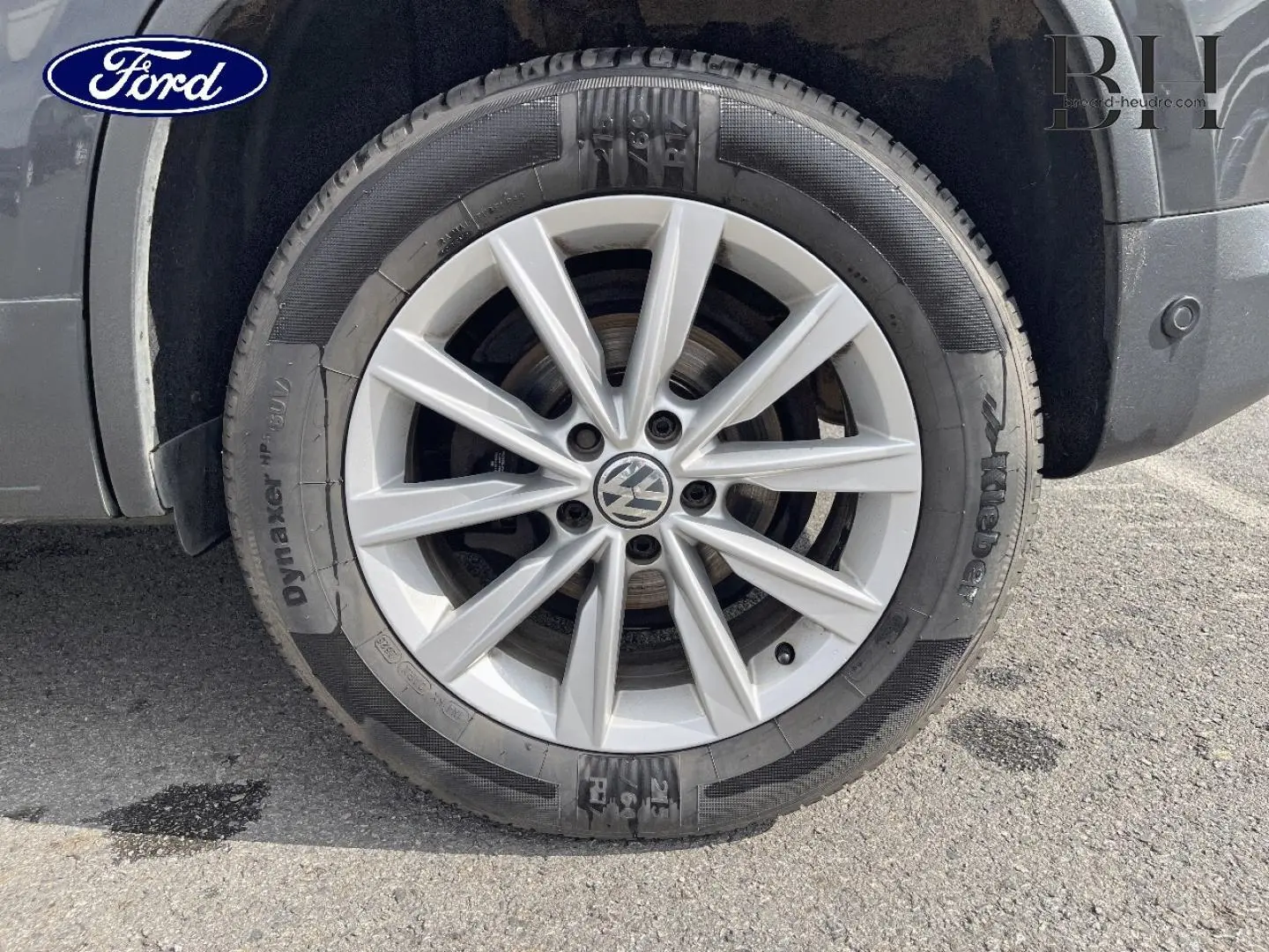 Gros plan sur la jante alu argentée avec logo Volkswagen, montée sur un pneu noir, partie arrière droite du Tiguan gris poivre.