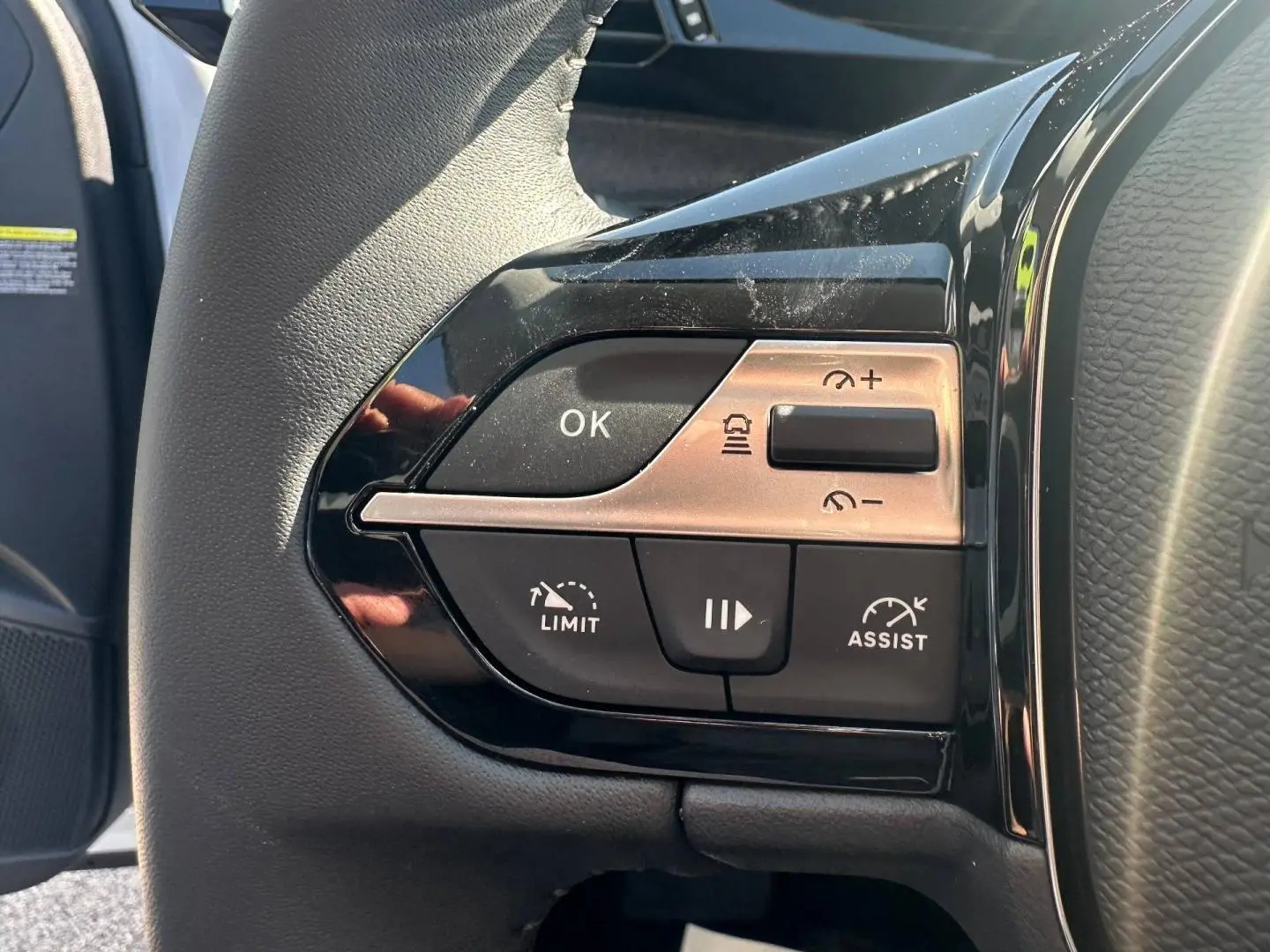 Gros plan sur les commandes de régulateur de vitesse au volant noir du Peugeot 308 SW hybride blanc Okénite.