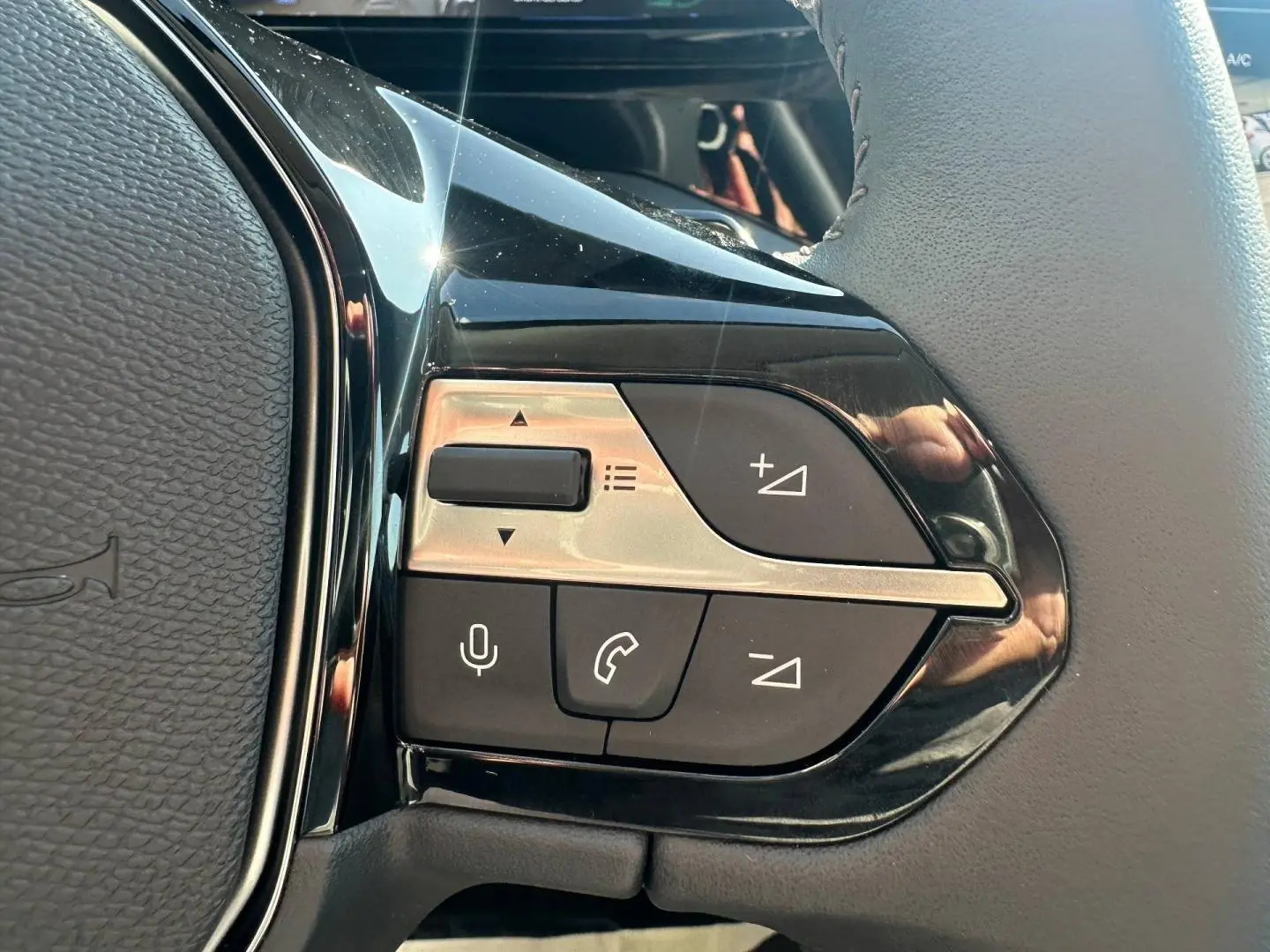 Gros plan sur les commandes multifonctions noires et argentées du volant d’une Peugeot 308 SW hybride blanche.