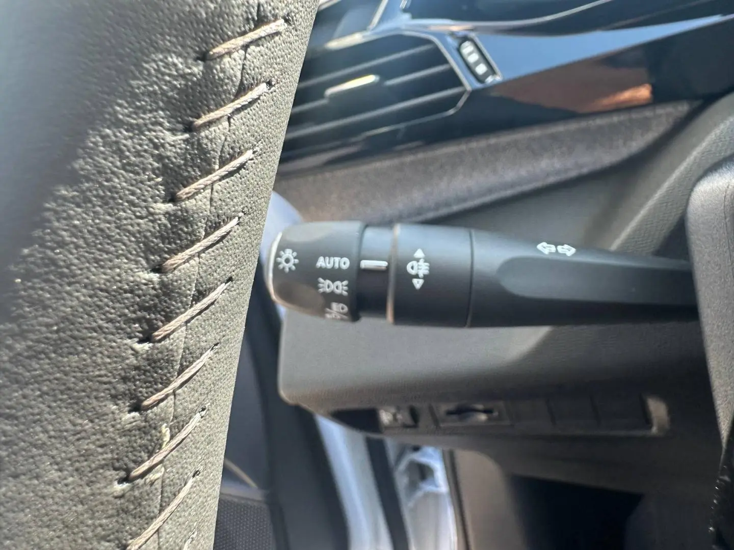 Gros plan sur la commande des phares et clignotants à gauche du volant dans l'habitacle d'une Peugeot 308 SW blanche.