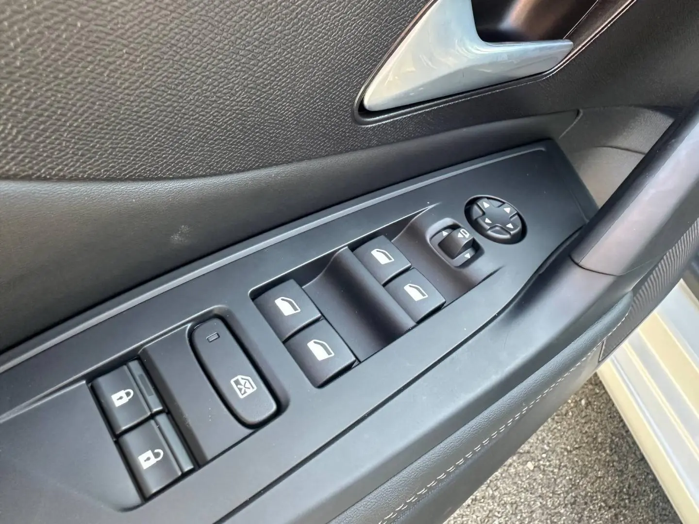 Gros plan sur la commande des vitres et rétroviseurs côté conducteur d’une Peugeot 308 SW blanche.