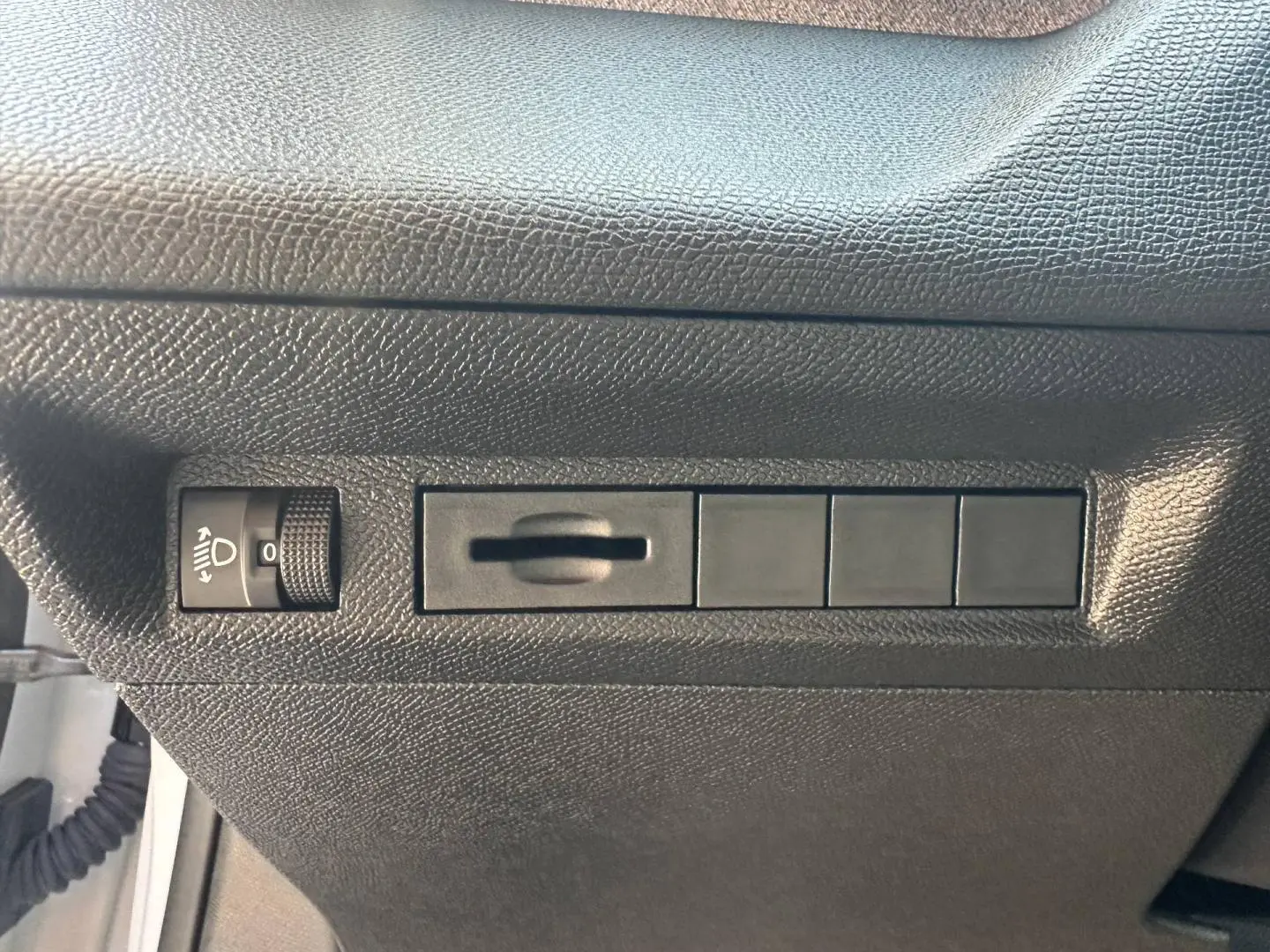 Détail du tableau de bord côté gauche noir texturé avec commande de réglage des phares sur Peugeot 308 SW blanc.