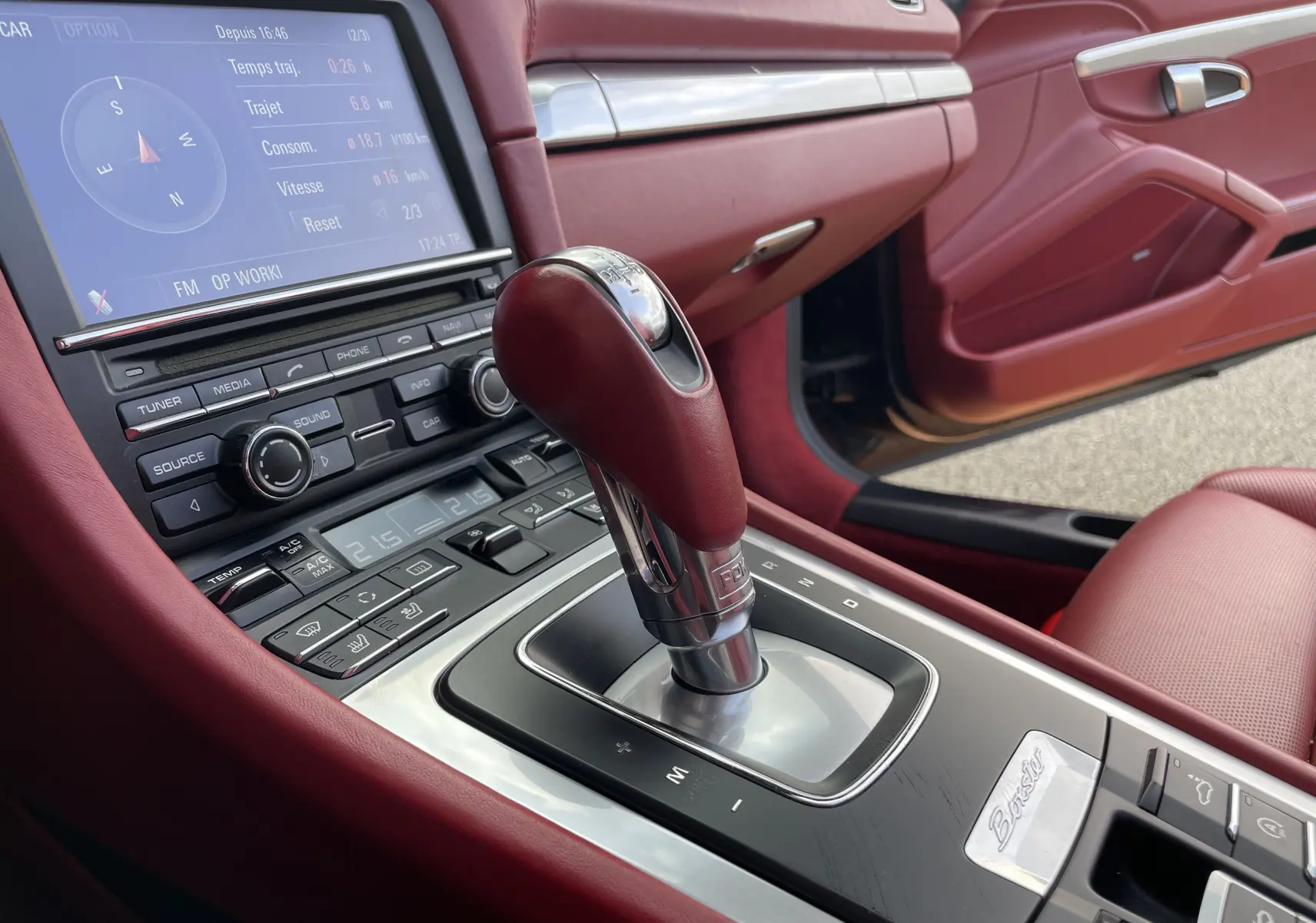 Gros plan sur la console centrale rouge grenat de la Porsche Boxster S 981 avec levier de vitesse PDK et écran tactile affichant la navigation.