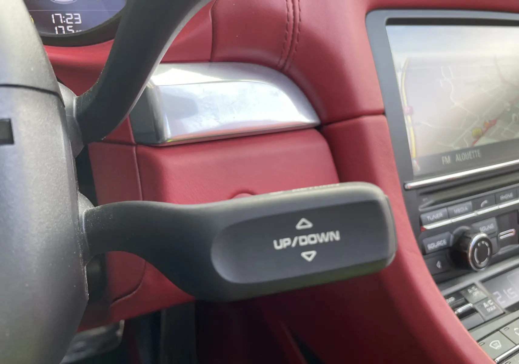 Gros plan sur la commande au volant avec inscription up/down, intérieur cuir rouge grenat et écran de navigation Porsche visible.