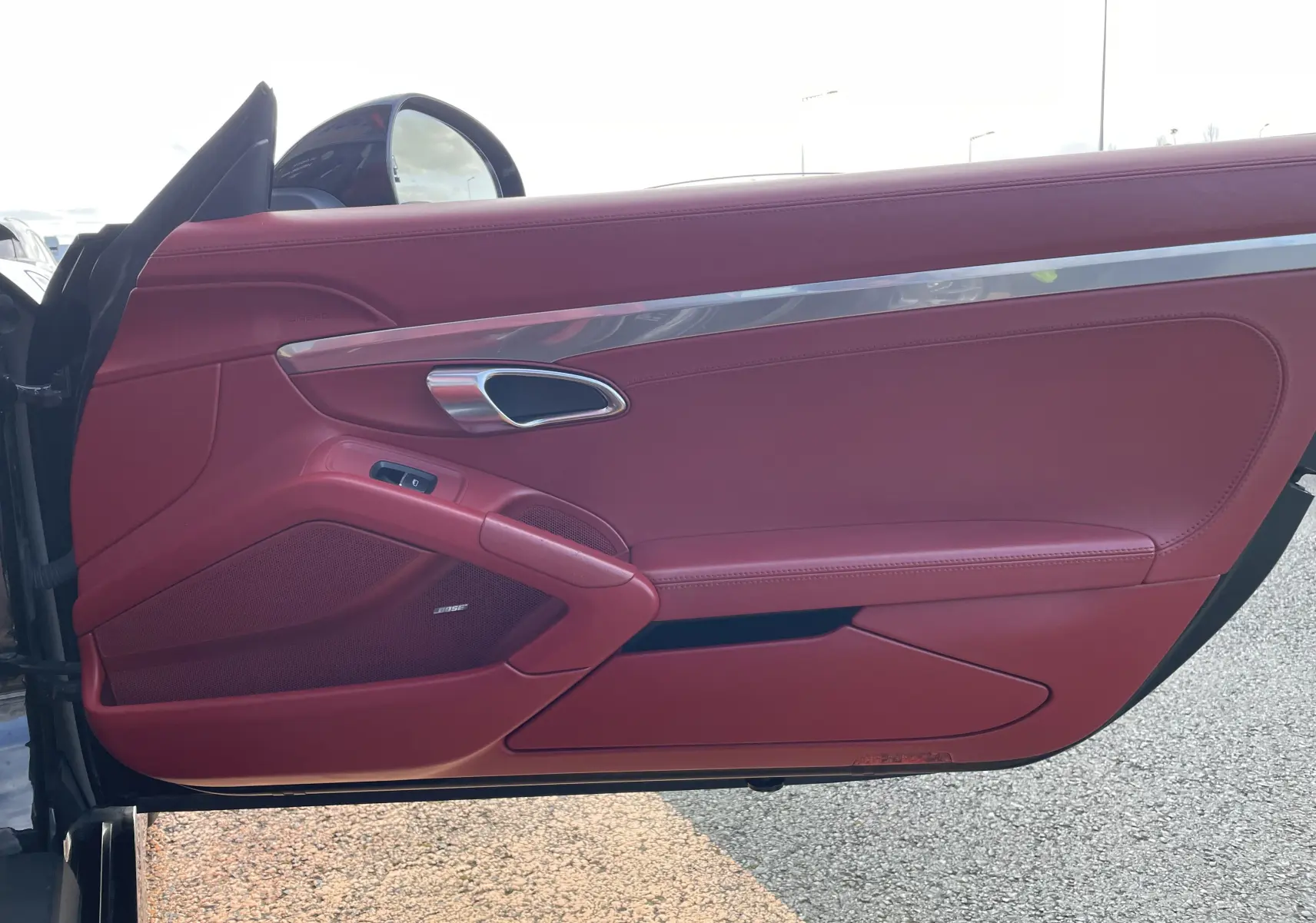 Gros plan sur la porte côté gauche de la Porsche Boxster S 981 2012, cuir rouge grenat avec haut-parleur Bose intégré.