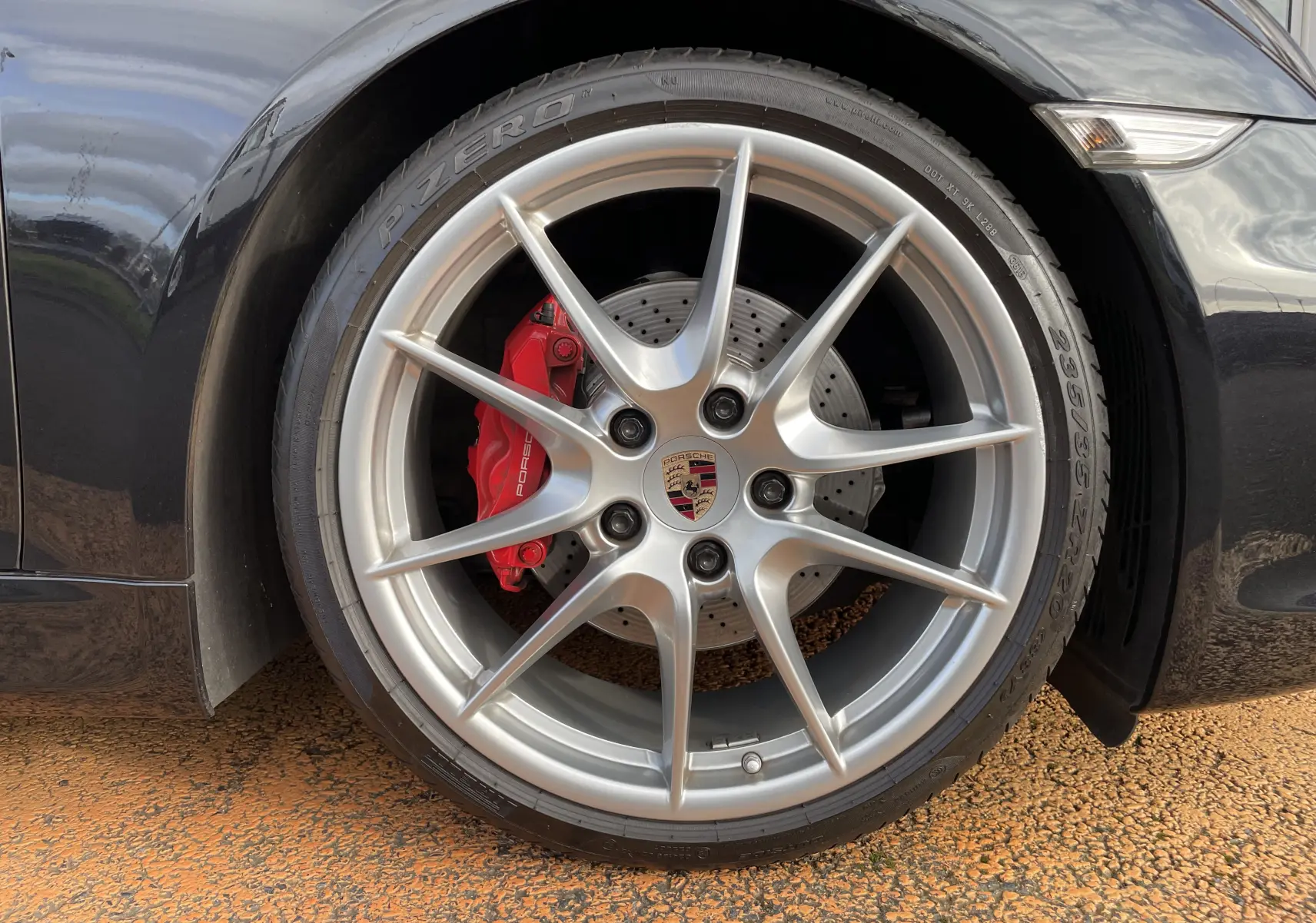 Gros plan sur la jante avant droite argentée d'une Porsche Boxster S noire avec étrier de frein rouge visible.