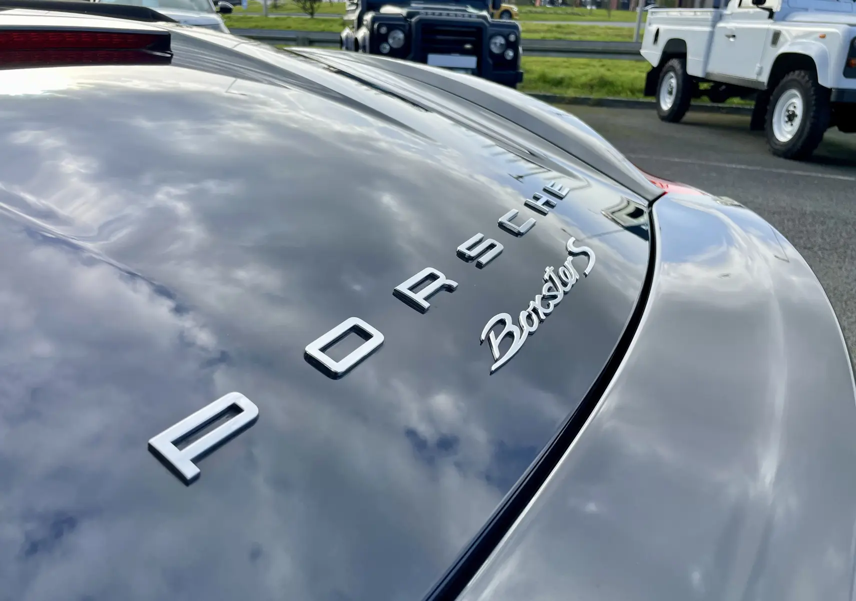 Gros plan sur l'arrière noir intense brillant d'une Porsche Boxster S, mettant en valeur le logo et l'inscription du modèle.