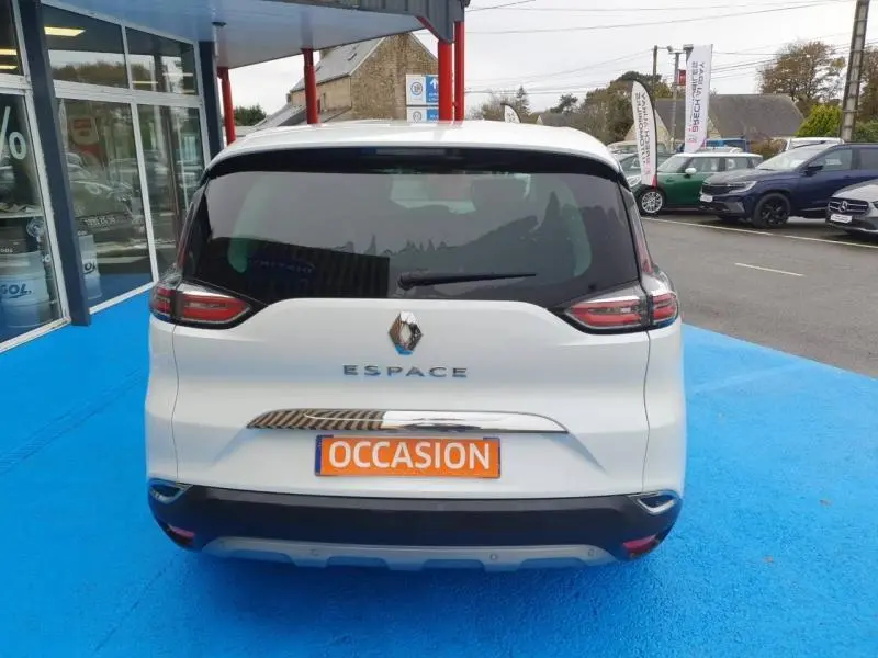 Vue arrière d'un Renault Espace blanc nacré avec plaque "OCCASION" sur un sol bleu en concession.