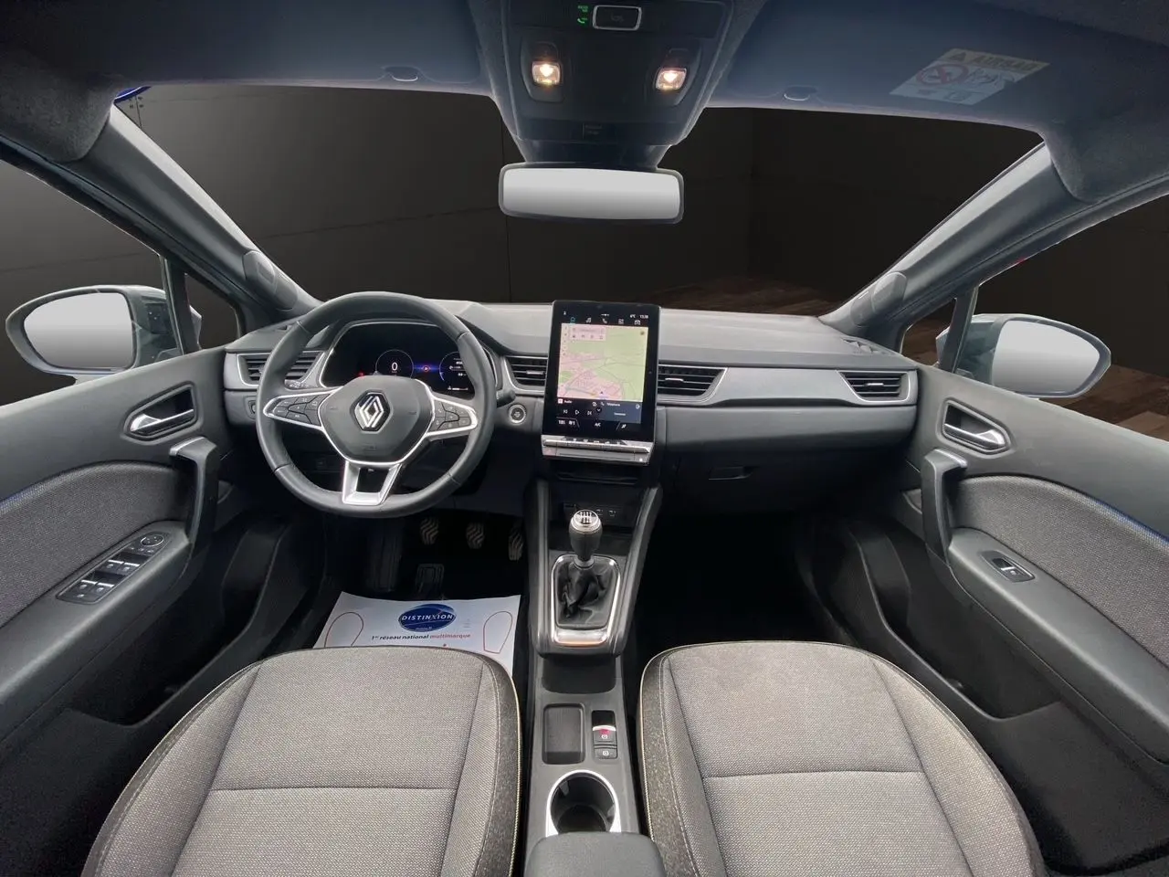 Vue intérieure avant du Renault Captur 2025 avec tableau de bord noir, écran tactile vertical et sièges tissu gris.