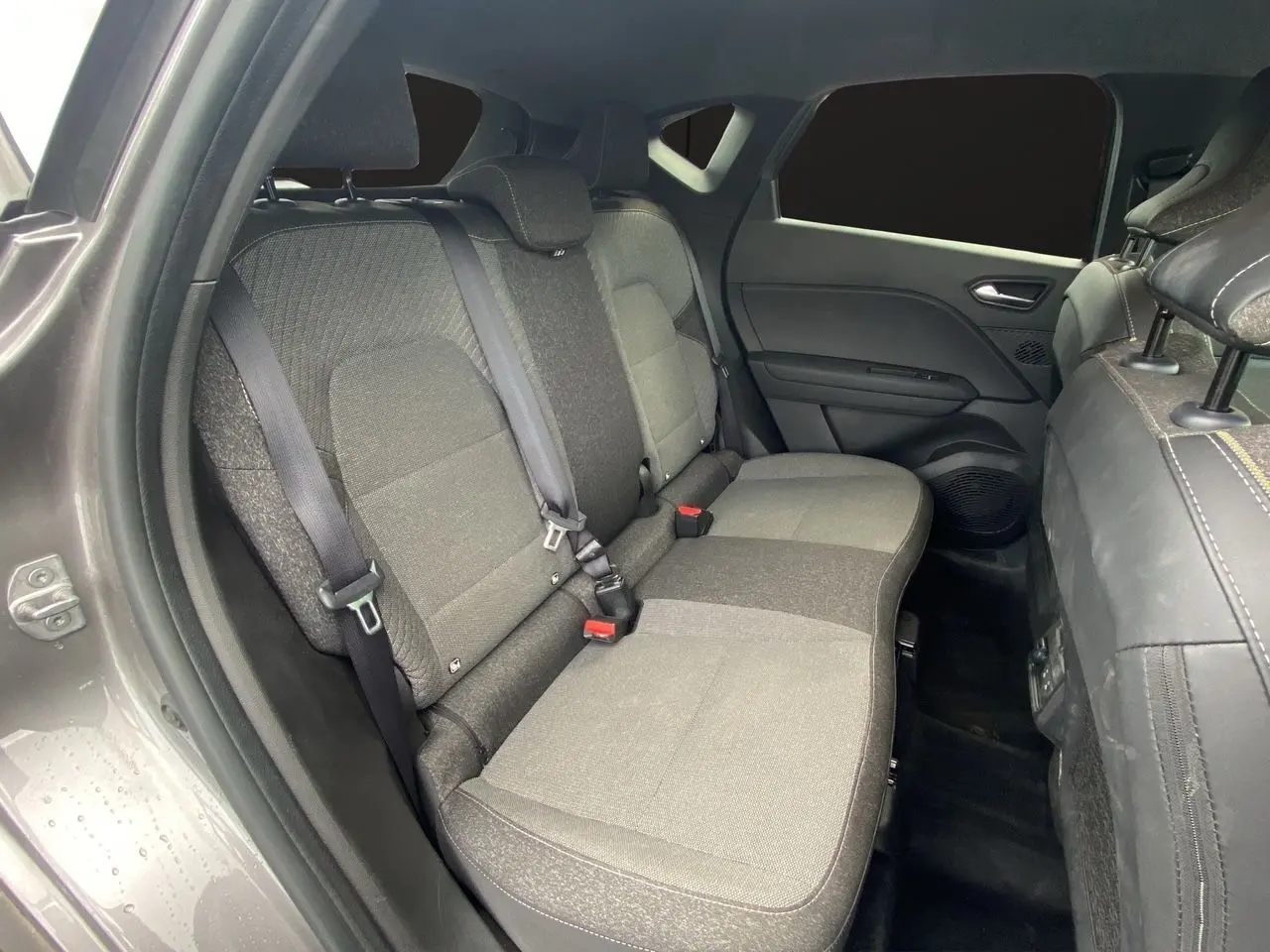 Vue intérieure côté gauche des sièges arrière gris tissu du Renault Captur 2025 avec ceinture de sécurité et porte fermé.