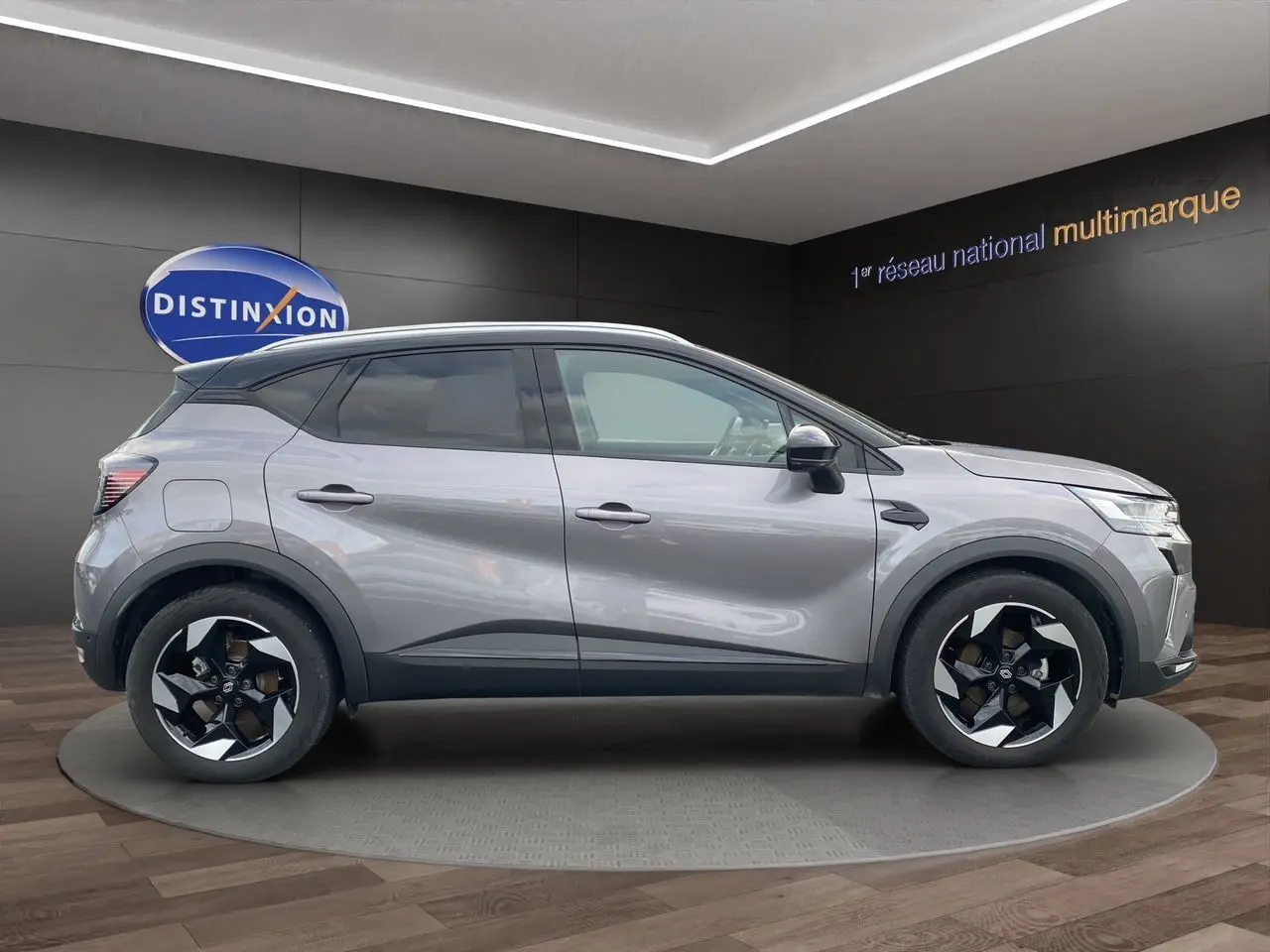 Profil droit du Renault Captur 2025 gris Cassiopée avec toit noir et jantes alu 18 pouces en intérieur showroom.