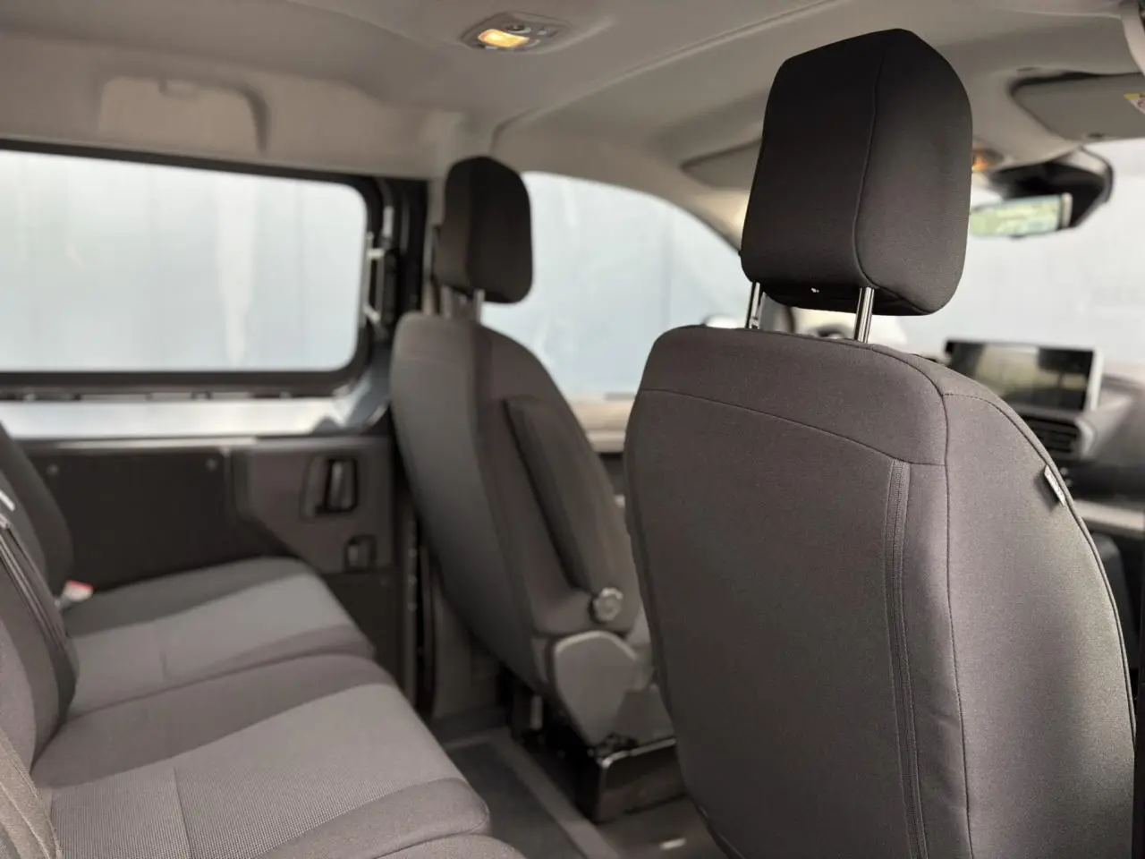 Vue intérieure côté droit du Citroën Jumpy XL 2025, montrant les sièges tissu bi-ton noir et gris et la banquette arrière.