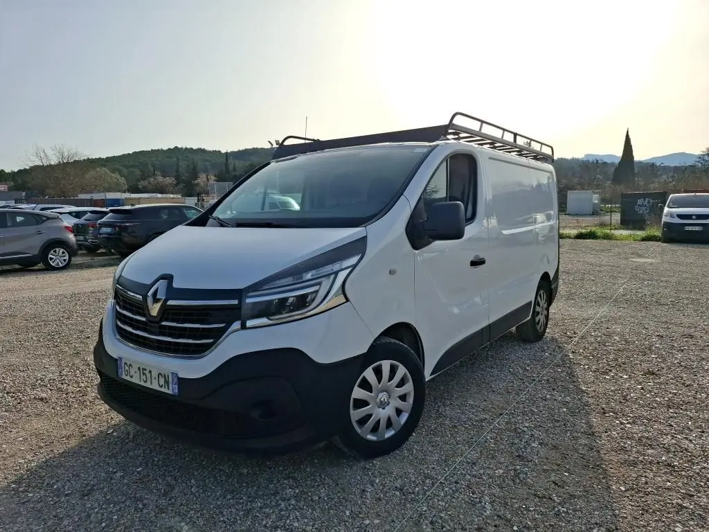 Renault Trafic Fourgon blanc vu en 3/4 avant droit avec galerie de toit et calandre noire distinctive.