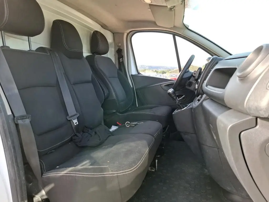 Vue intérieure côté conducteur du Renault Trafic Fourgon blanc 2021, montrant les sièges noirs et le tableau de bord.