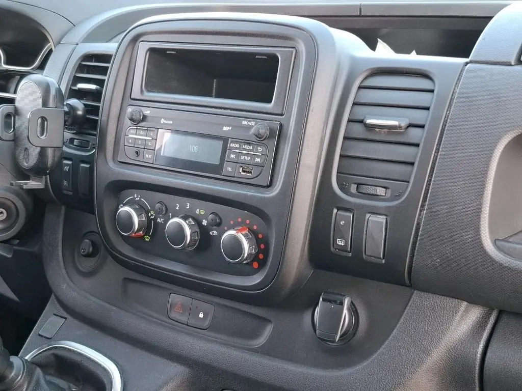 Vue rapprochée de la console centrale intérieure du Renault Trafic Fourgon blanc, avec commandes de climatisation et radio.