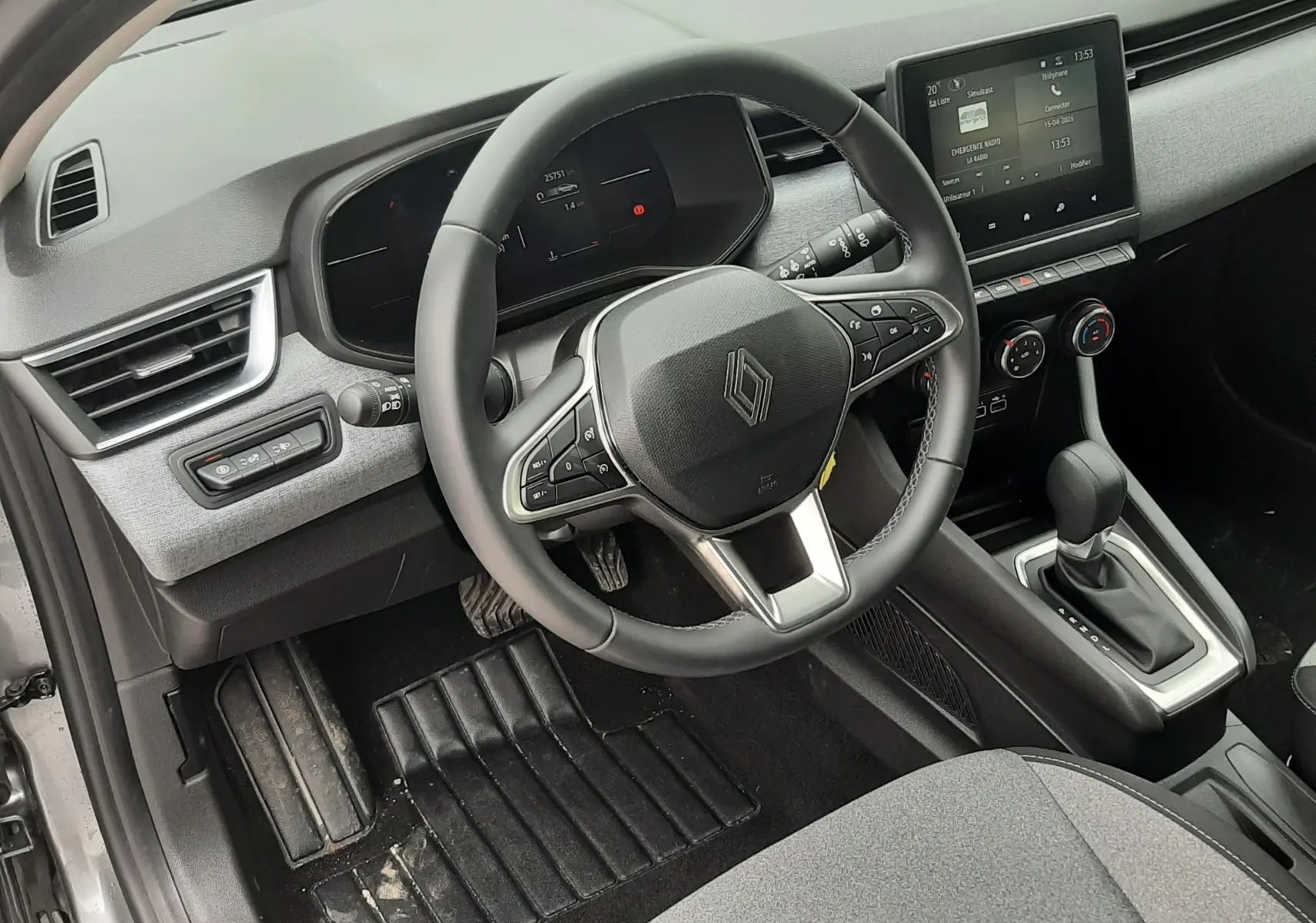 Vue intérieure côté conducteur de la Renault Clio V gris schiste, volant multifonction et écran tactile central visible.