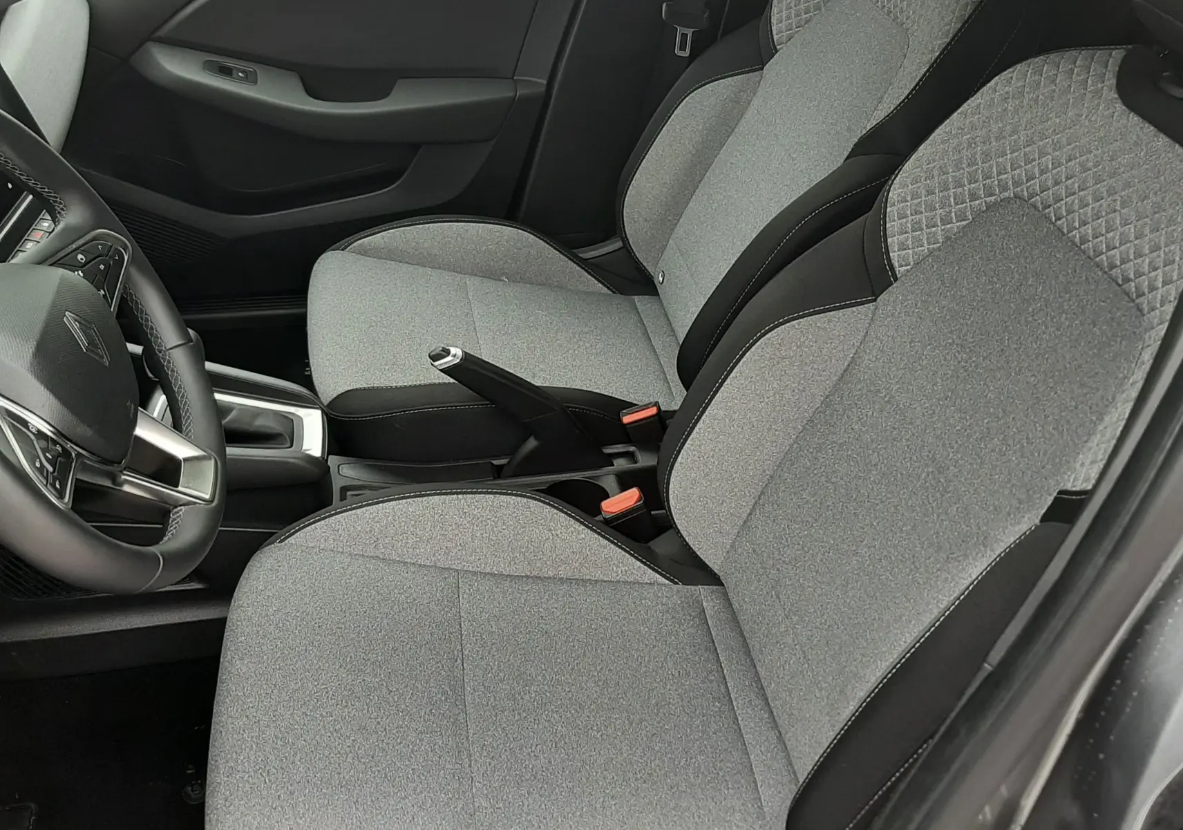 Vue intérieure côté conducteur de la Renault Clio V 2025, sièges tissu gris clair avec surpiqûres et détails noirs.