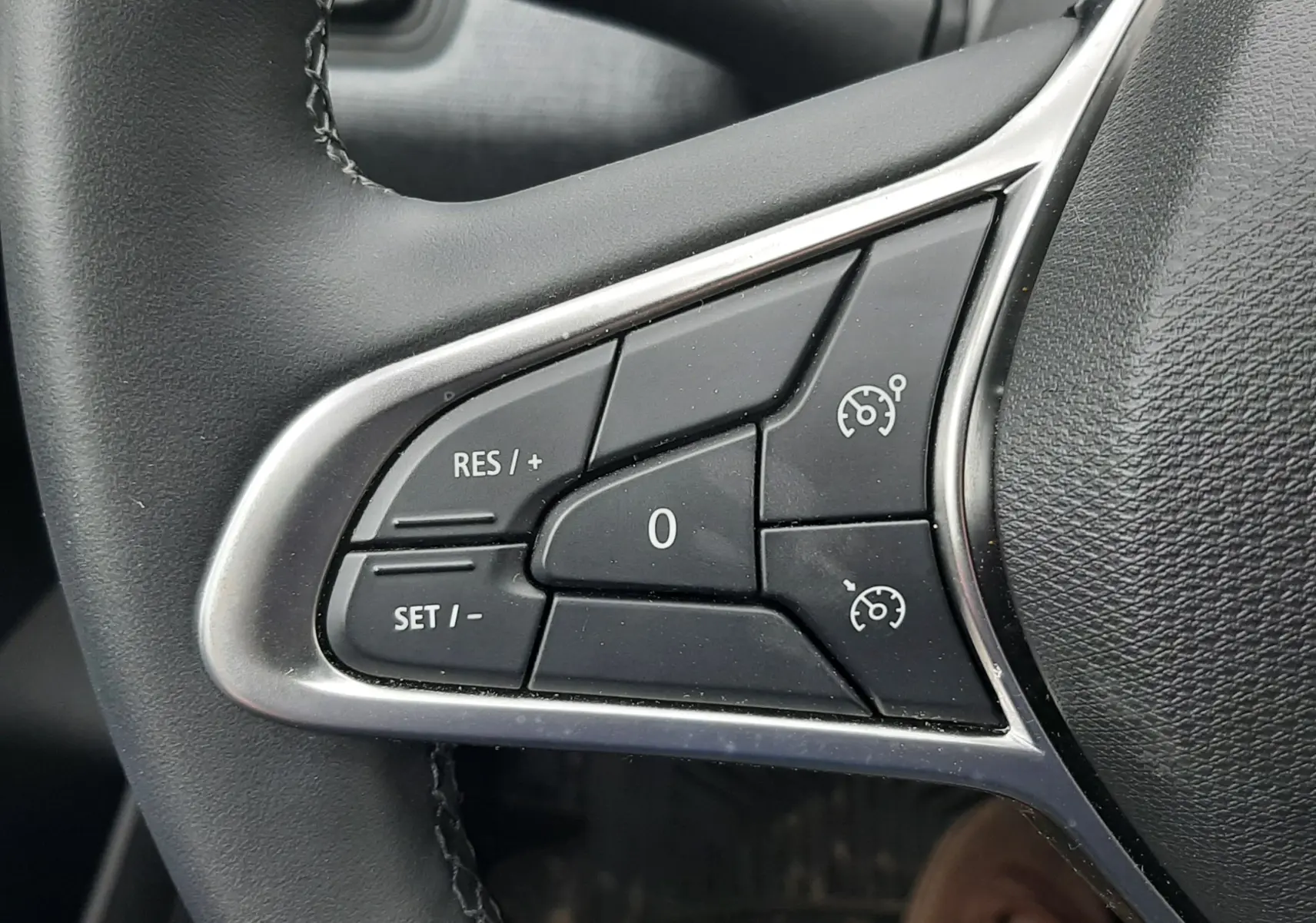 Gros plan sur les commandes de régulateur de vitesse au volant noir de la Renault Clio V gris schiste, côté gauche.
