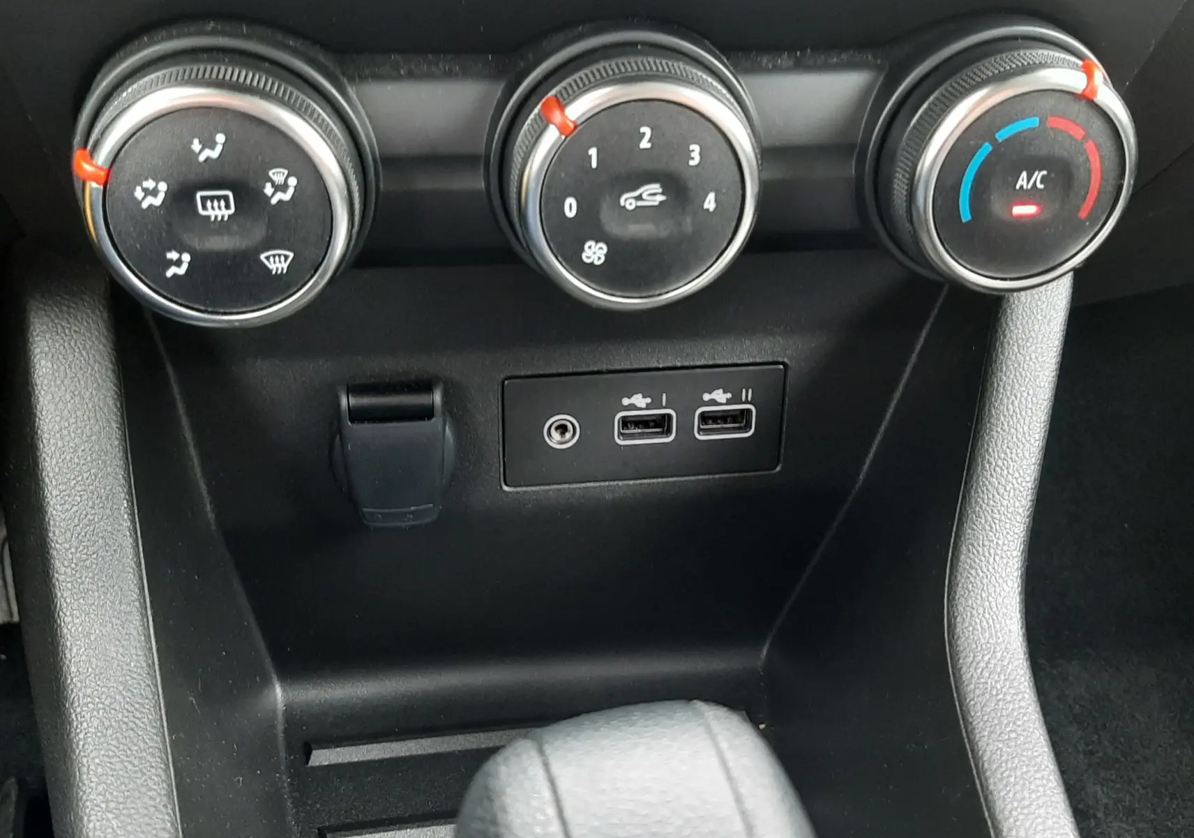 Gros plan sur les commandes de climatisation et ports USB du Renault Clio V gris schiste, version 2025, avec réglages manuels.