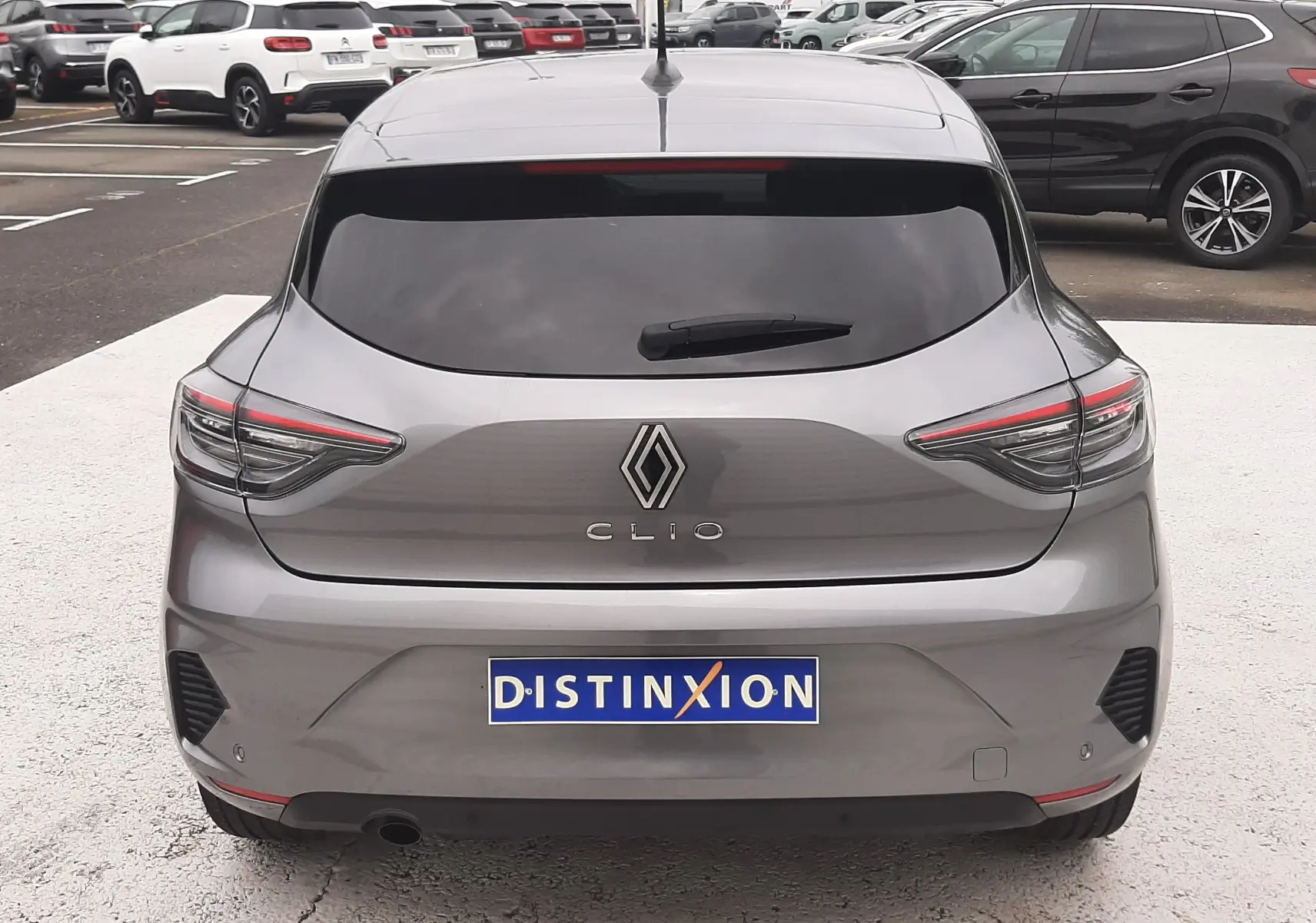 Vue arrière d'une Renault Clio V gris schiste avec feux LED fins et lunette arrière teintée, stationnée en extérieur.