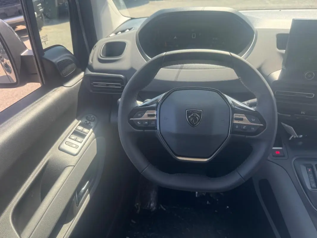 Vue intérieure centrée sur le volant cuir multifonctions du Peugeot Rifter gris avec tableau de bord et commandes côté gauche.