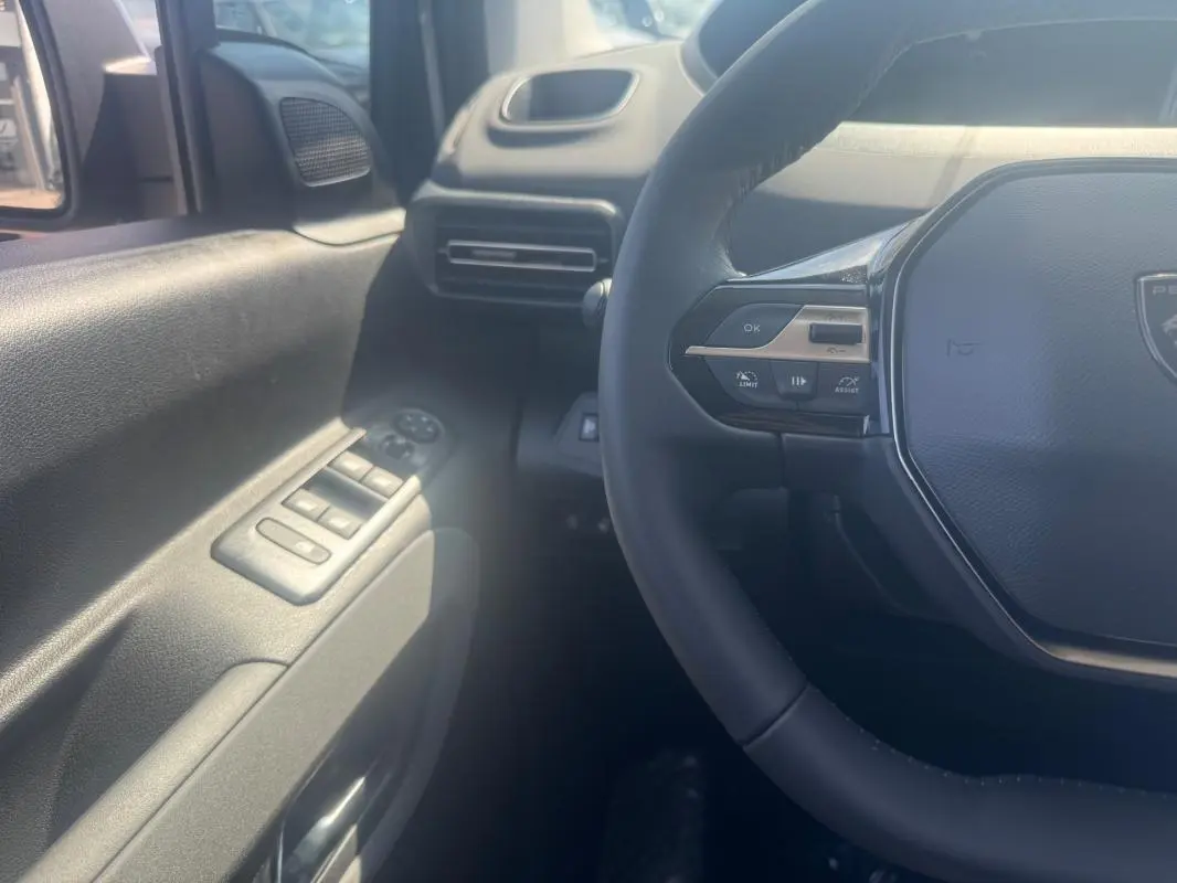 Vue intérieure côté conducteur du Peugeot Rifter gris 2026, volant multifonctions et commandes des vitres visibles.