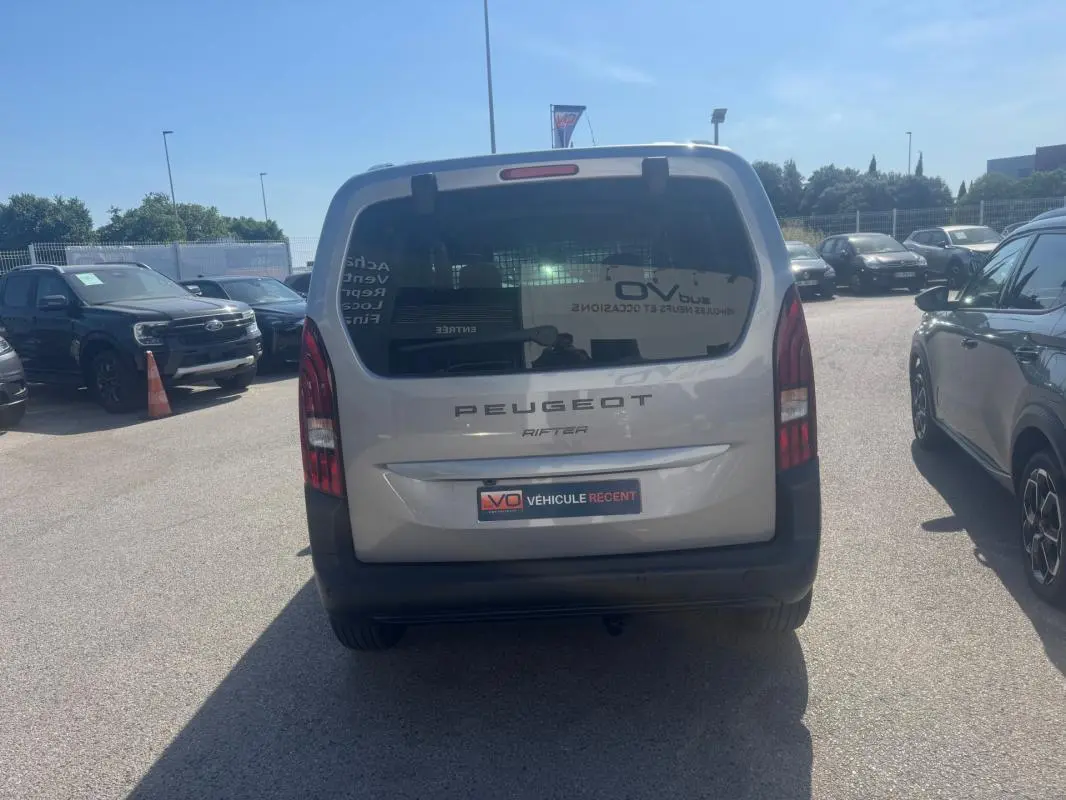 Vue arrière d'un Peugeot Rifter gris 2026 avec porte latérale et barres de toit visibles en extérieur.