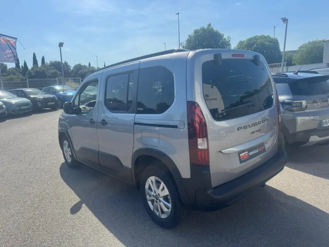 Vue 3/4 arrière droite d’un Peugeot Rifter gris 2026 avec barres de toit et jantes alliage 17 pouces.