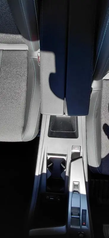 Vue plongeante sur la console centrale noire du Peugeot 408 Hybrid 145 e-DCS6 Allure avec accoudoir et porte-gobelets.