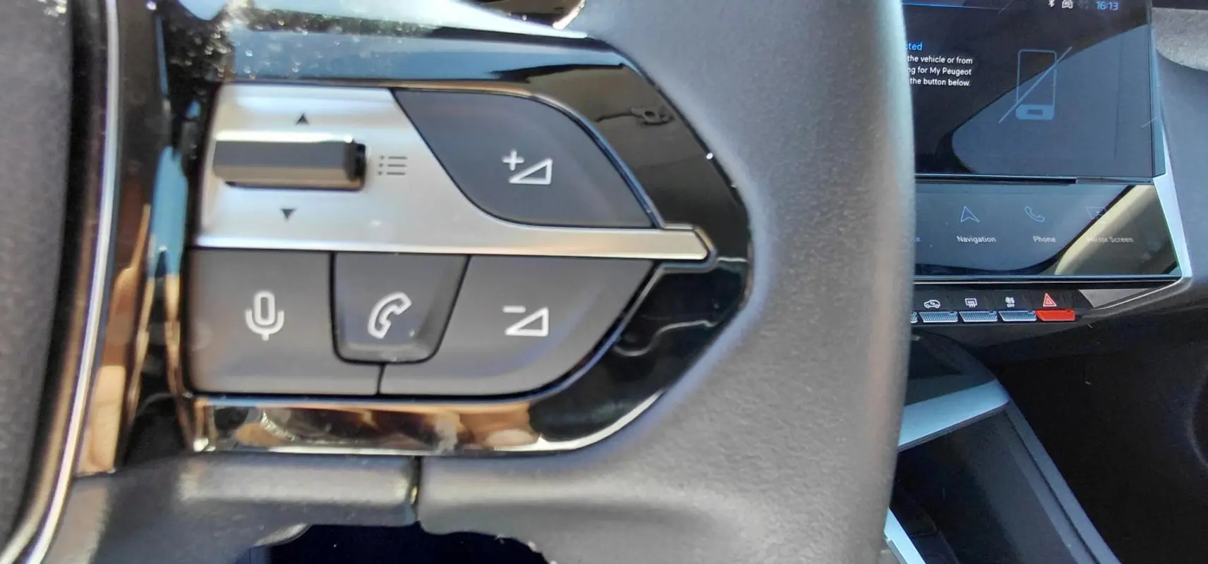 Gros plan sur les commandes au volant noir du Peugeot 408 Hybrid 145 e-DCS6 Allure 2025, avec écran tactile en arrière-plan.