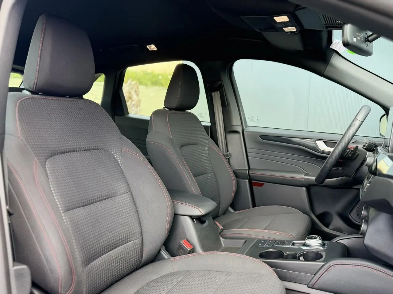 Vue intérieure côté droit du Ford Kuga 2023 noir Agathe, sièges tissu noirs avec surpiqûres rouges et console centrale.