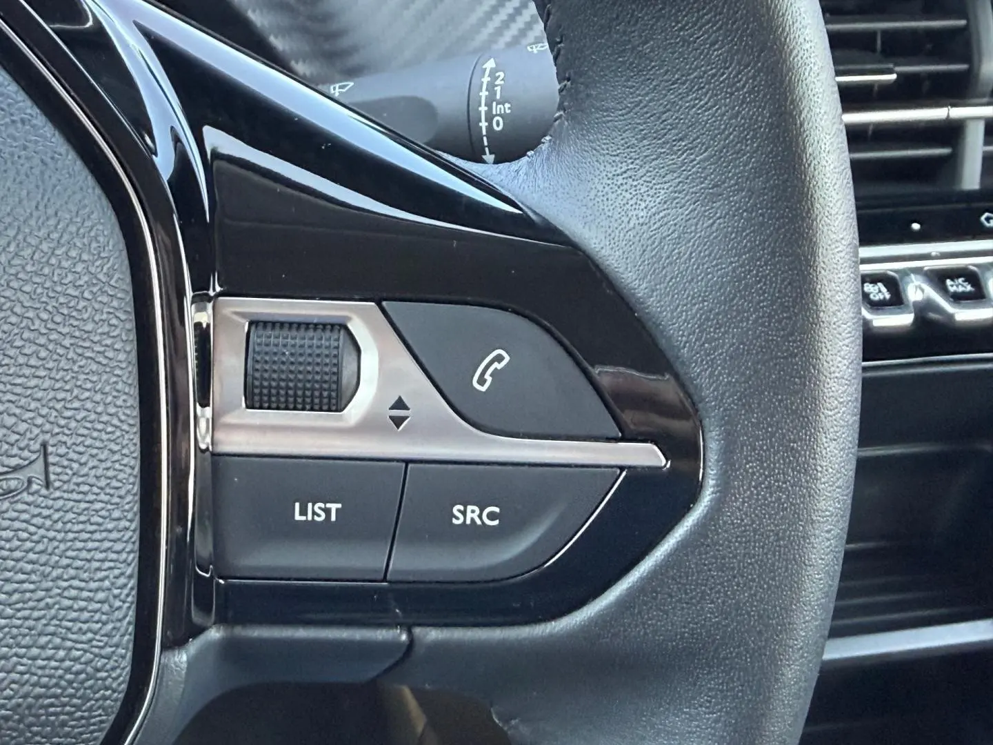 Gros plan sur les commandes audio au volant noir de la Peugeot 208 1.2 100ch Style, avec molette et boutons SRC et LIST.