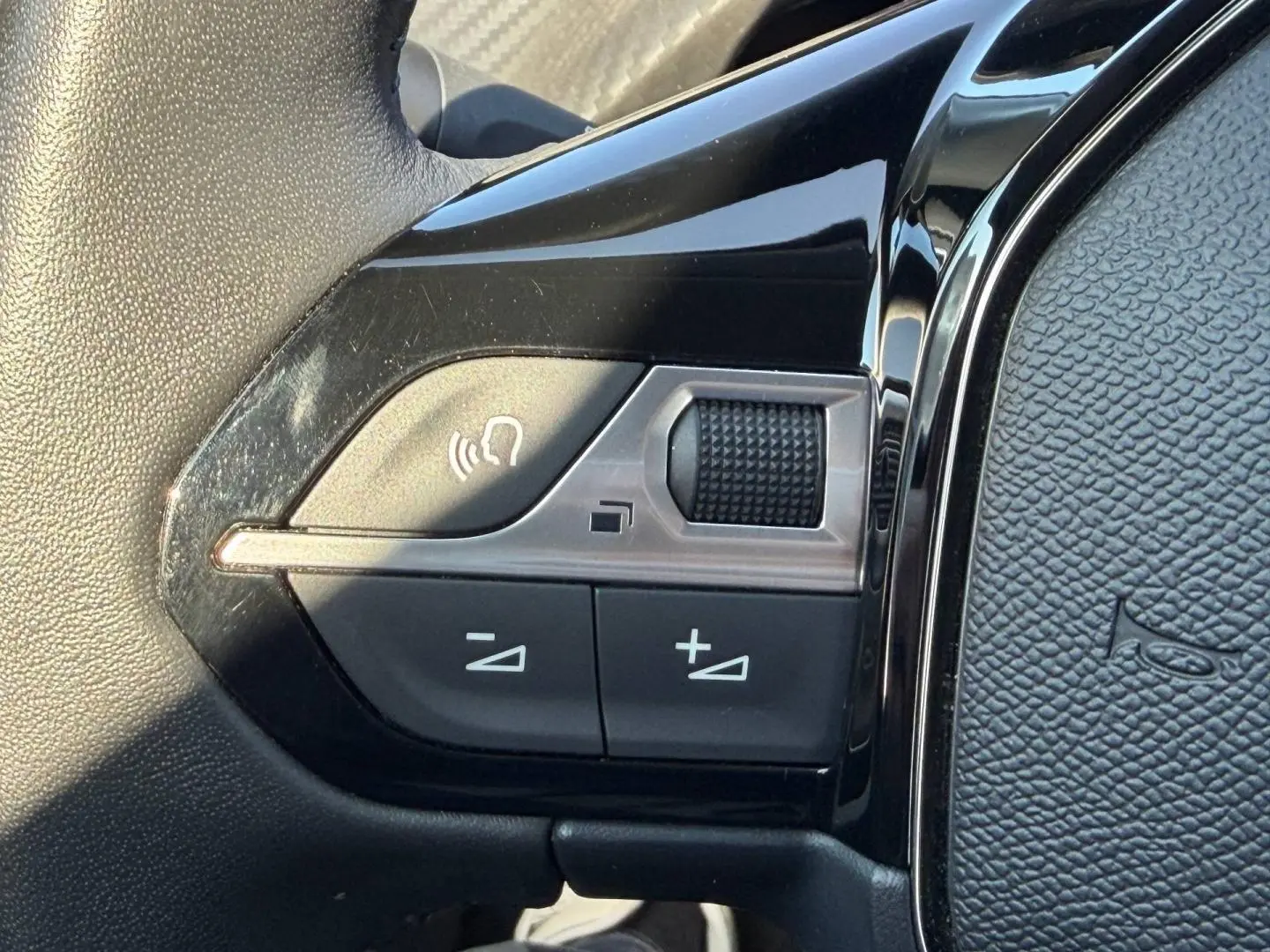 Gros plan sur les commandes vocales et volume sur le volant noir brillant de la Peugeot 208 2025.