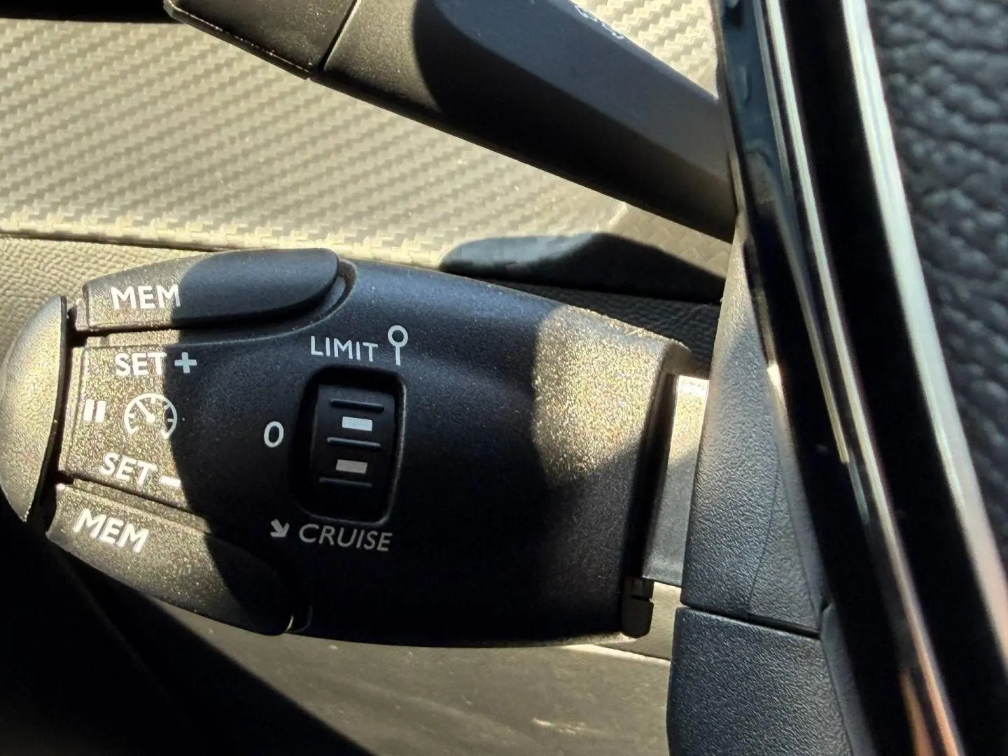 Gros plan sur la commande de régulateur de vitesse noire à gauche du volant dans l’habitacle d’une Peugeot 208 noire.