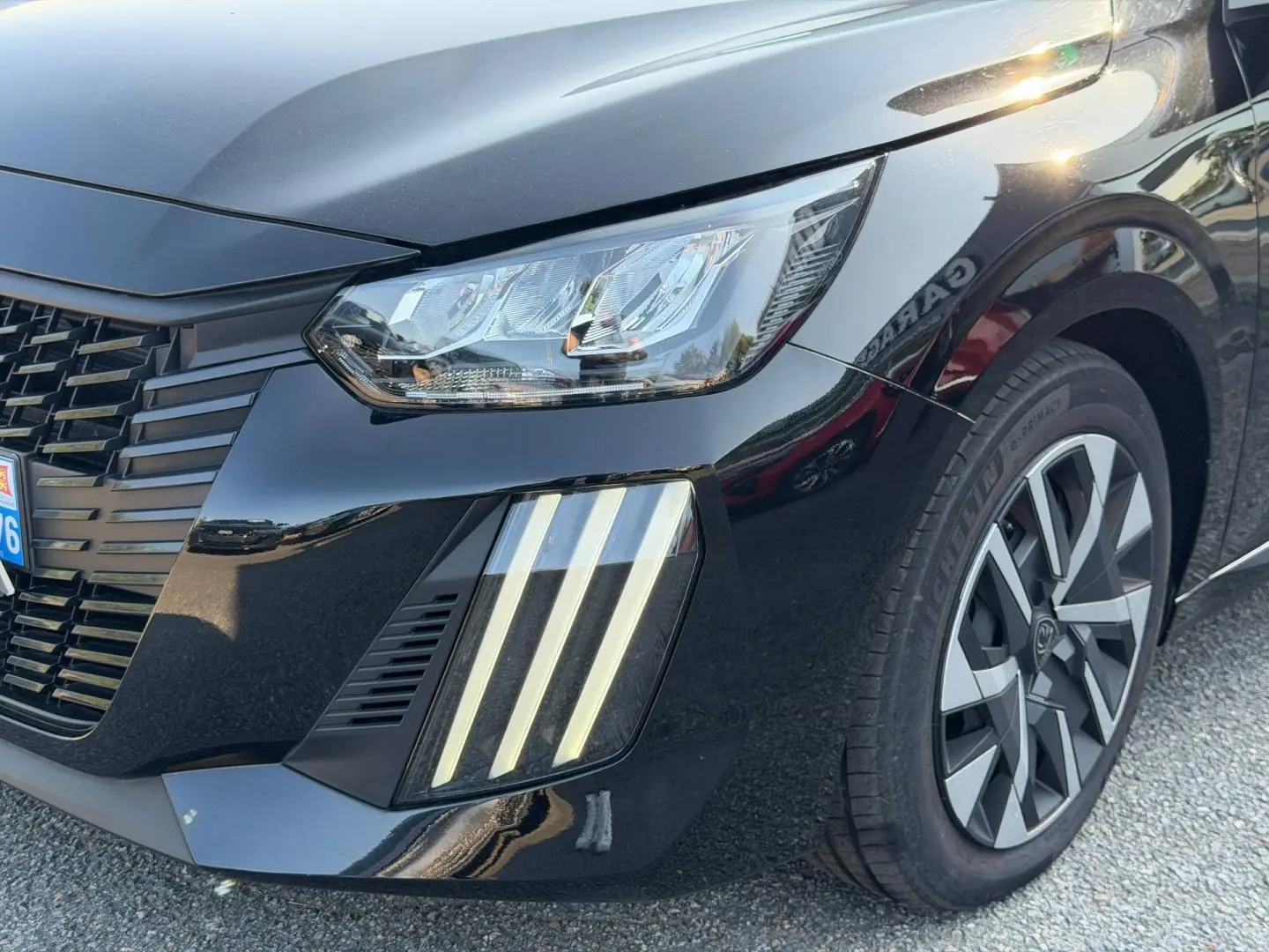 Gros plan sur l'avant droit d'une Peugeot 208 noire Perla Nera avec phares LED et jante alliage distinctive.