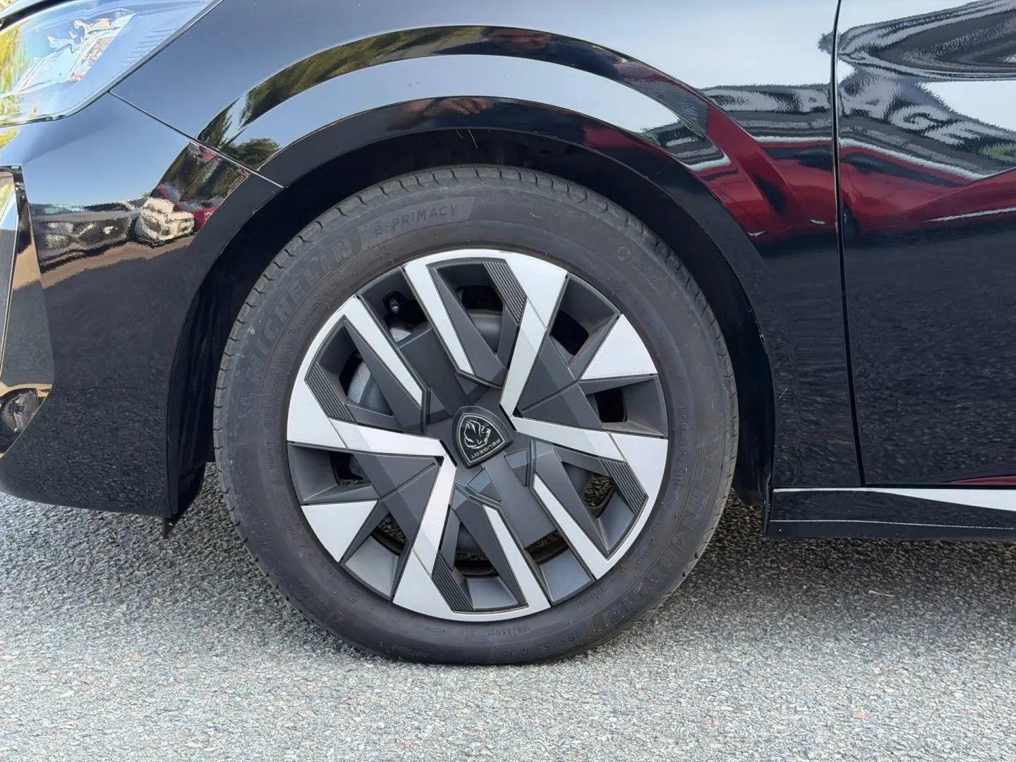 Gros plan sur la roue avant gauche de la Peugeot 208 noire Perla Nera avec jante au design géométrique moderne.