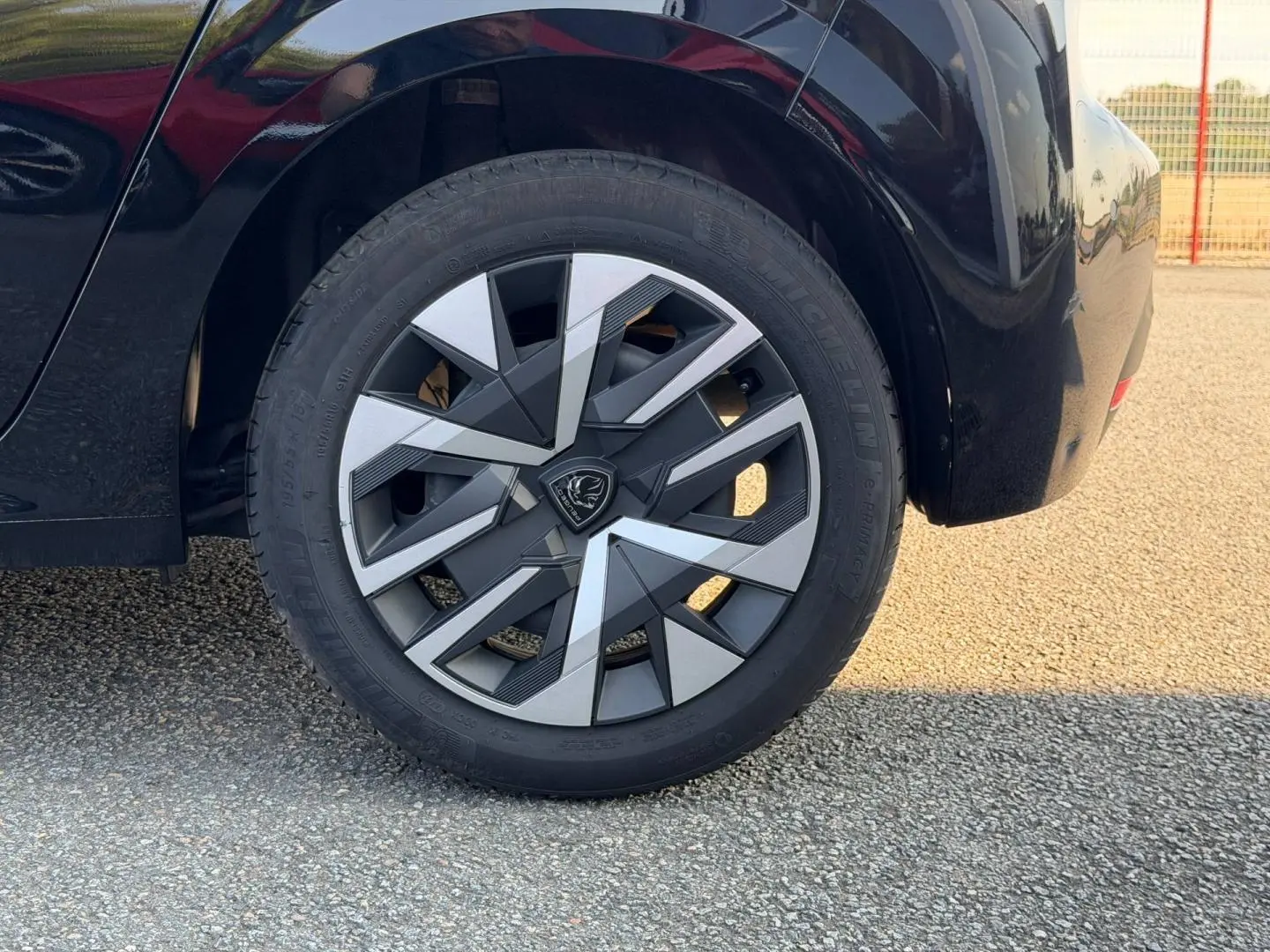Gros plan sur la roue arrière droite noire Perla Nera d'une Peugeot 208 1.2 100ch avec jante au design géométrique bicolore.