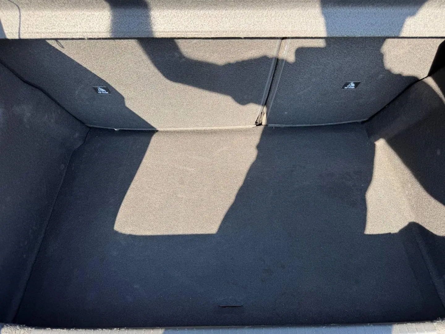Coffre vide vu de dessus, revêtement tissu noir, banquette arrière rabattable visible en arrière-plan.