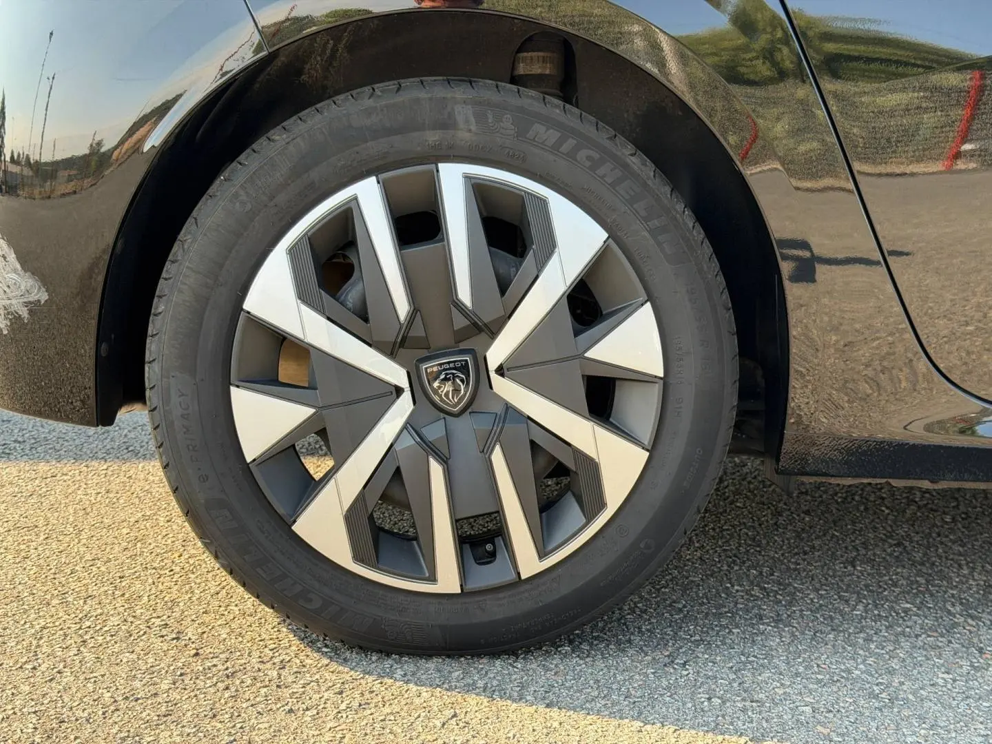 Gros plan sur la roue avant gauche d'une Peugeot 208 noire Perla Nera avec jante au design géométrique bicolore.