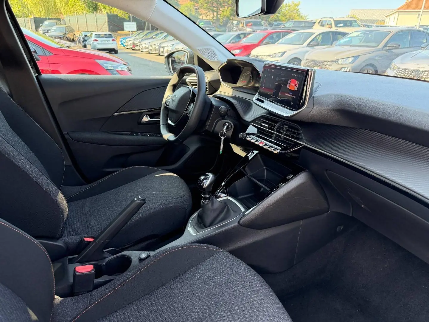 Vue intérieure côté conducteur de la Peugeot 208 1.2 100ch noire, avec tableau de bord moderne et boîte manuelle.